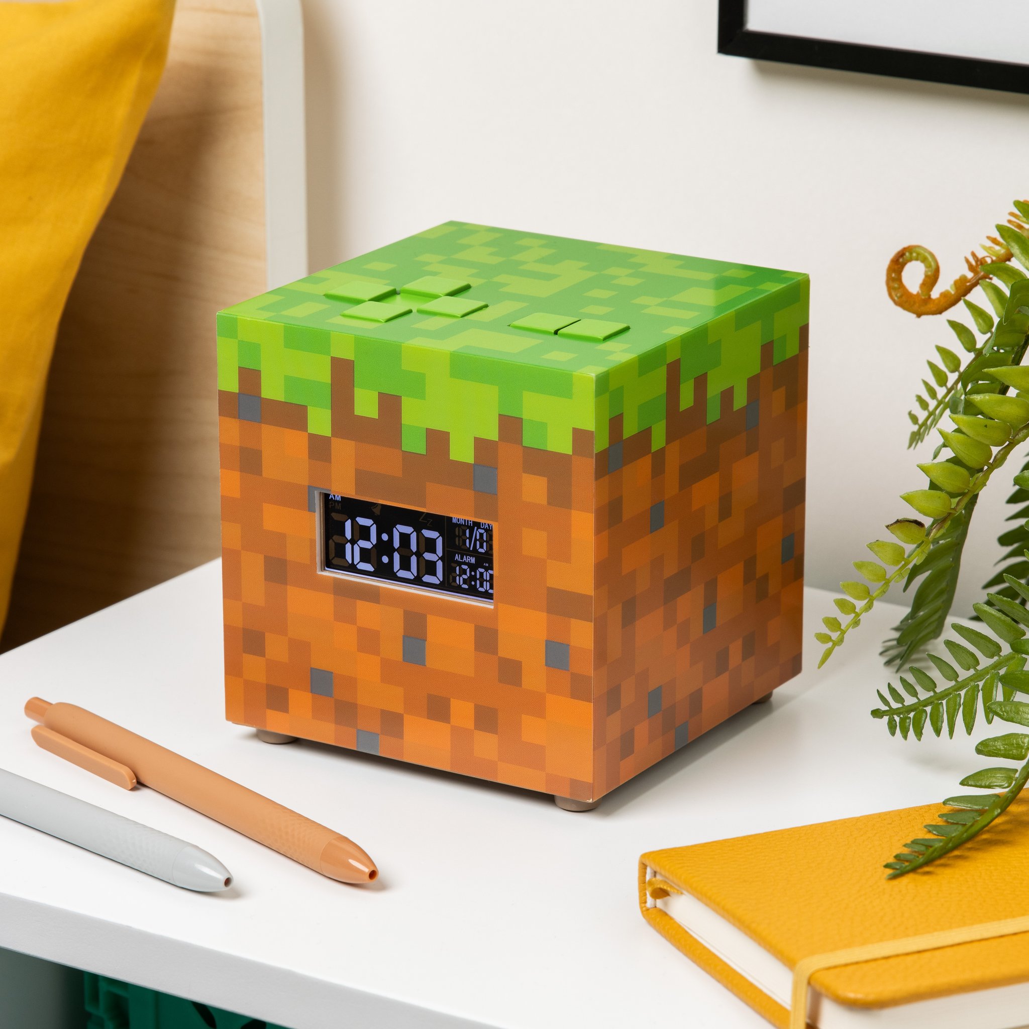 Minecraft grass block alarm clock on a desk next to a notebook and pens