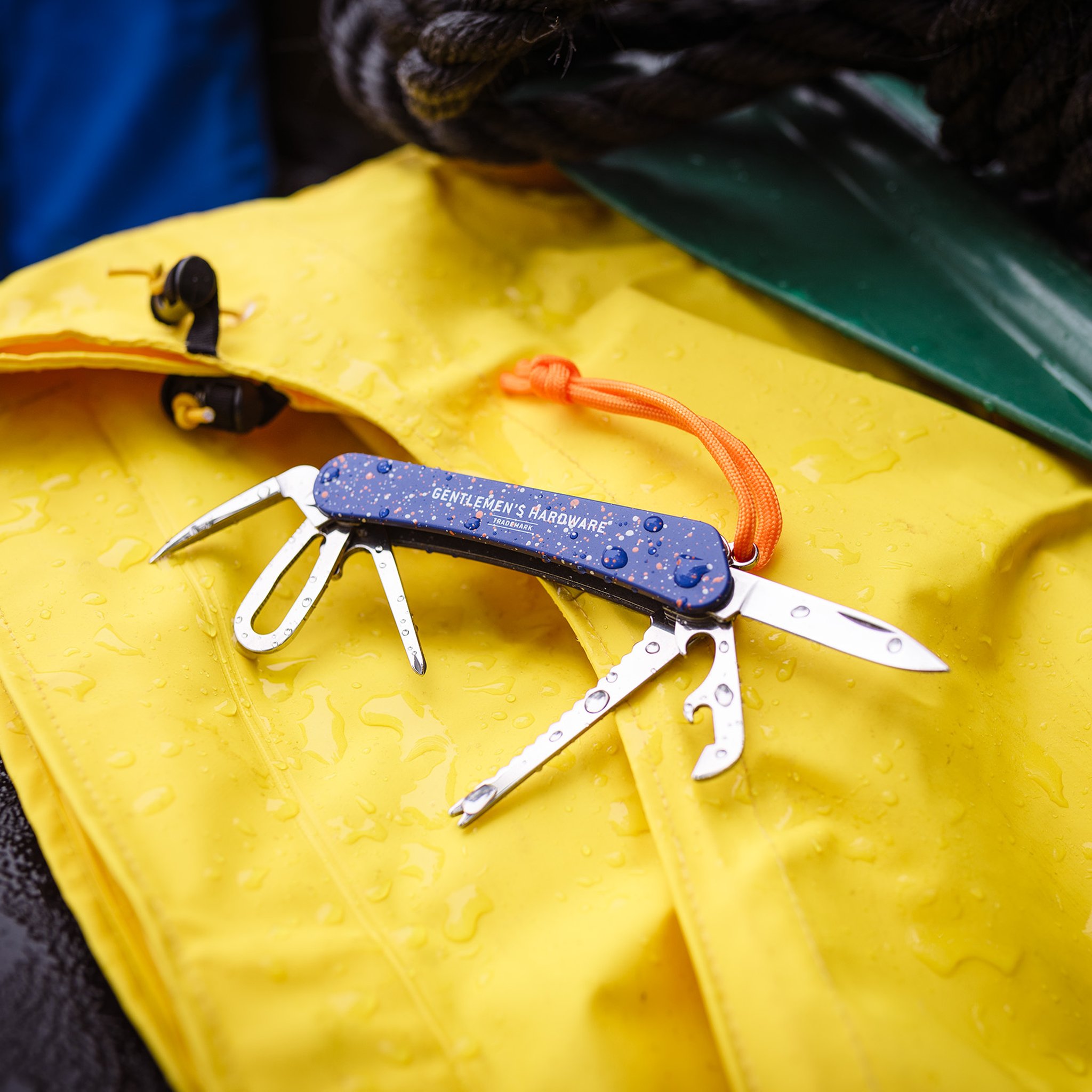 Marine Multitool liegt aufgeklappt auf einer gelben, regennassen Segeljacke, daneben dunkle Taue