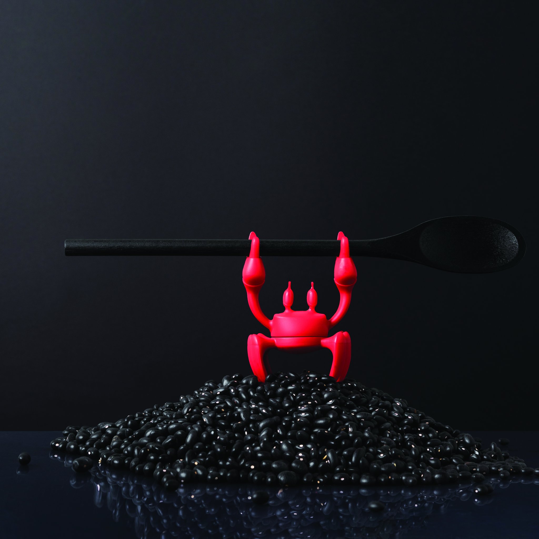 Red crab holding a spoon above black peppercorns