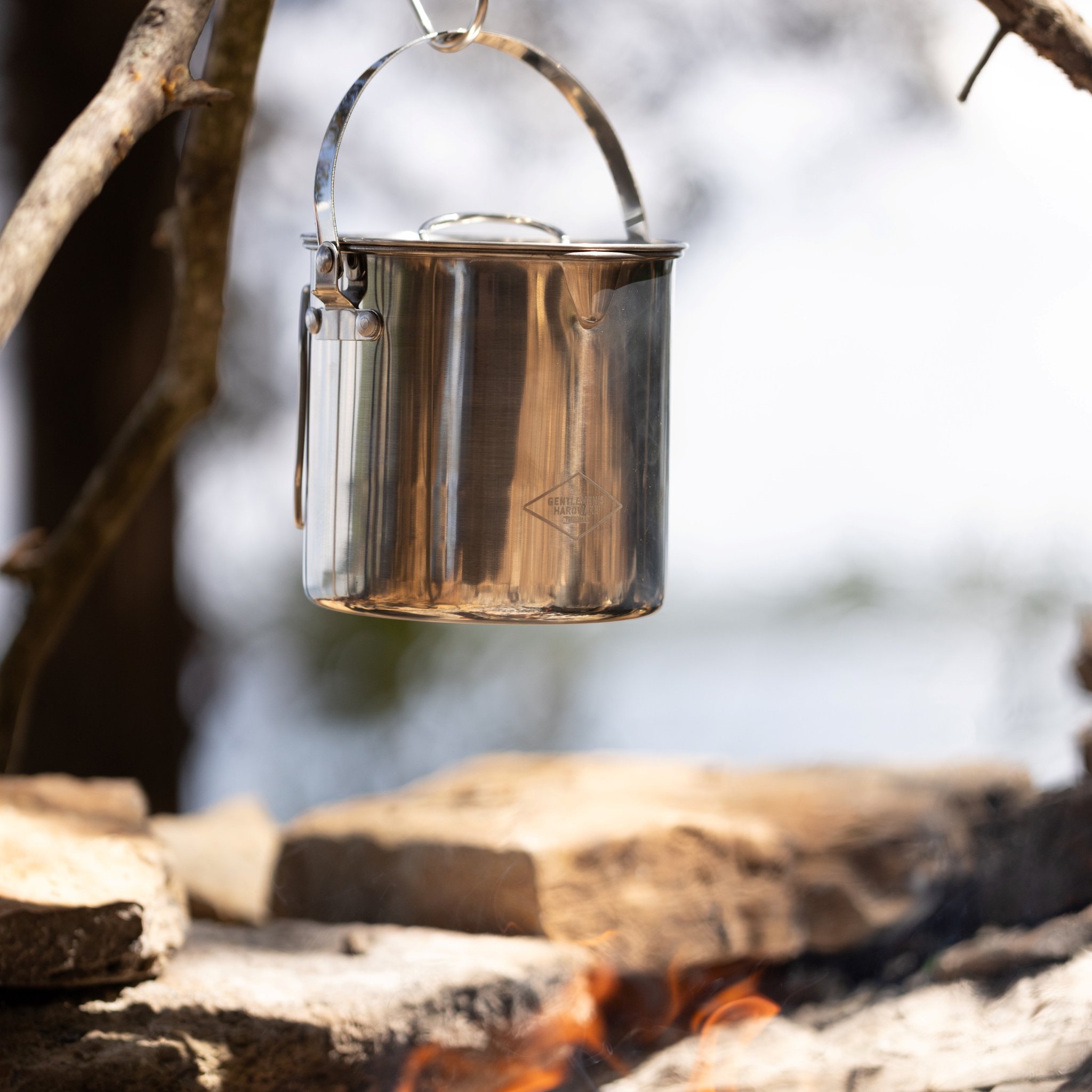 Close view of the hanging Campfire Cooking Pot with its raised bail handle, a logo on the side and embers below