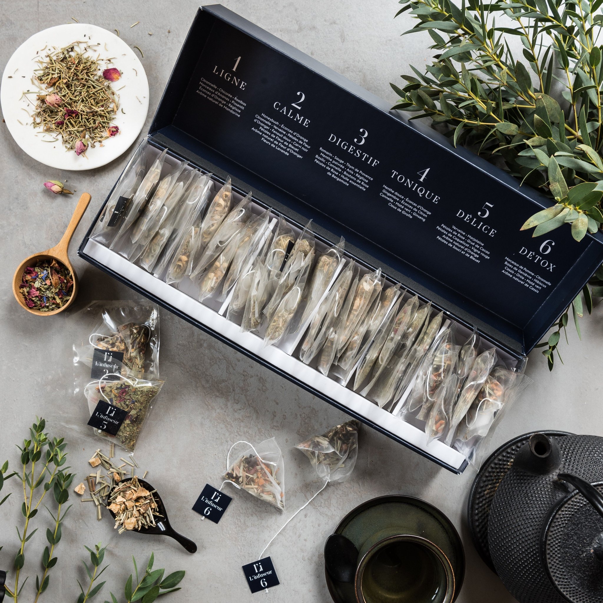 Coffret d'infusions sur une table en pierre avec herbes en vrac, sachets, théière en fonte et bol