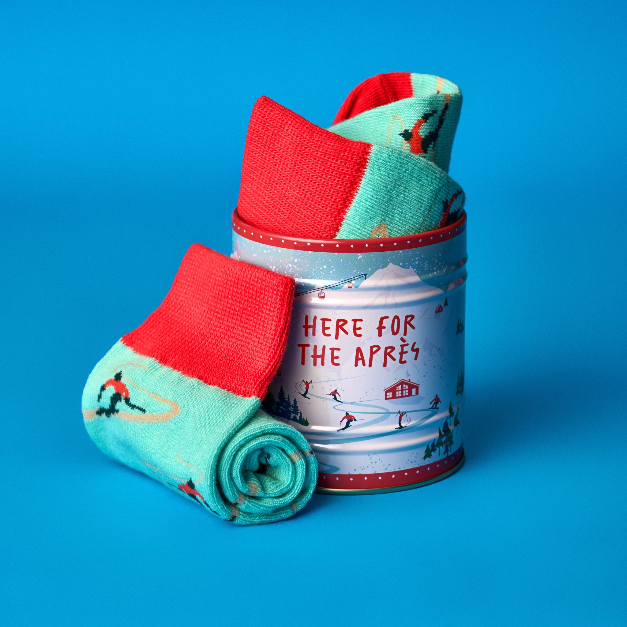 Socks in a Can - Skiing on a blue background: tin with socks inside and a rolled-up sock with skier pattern in front