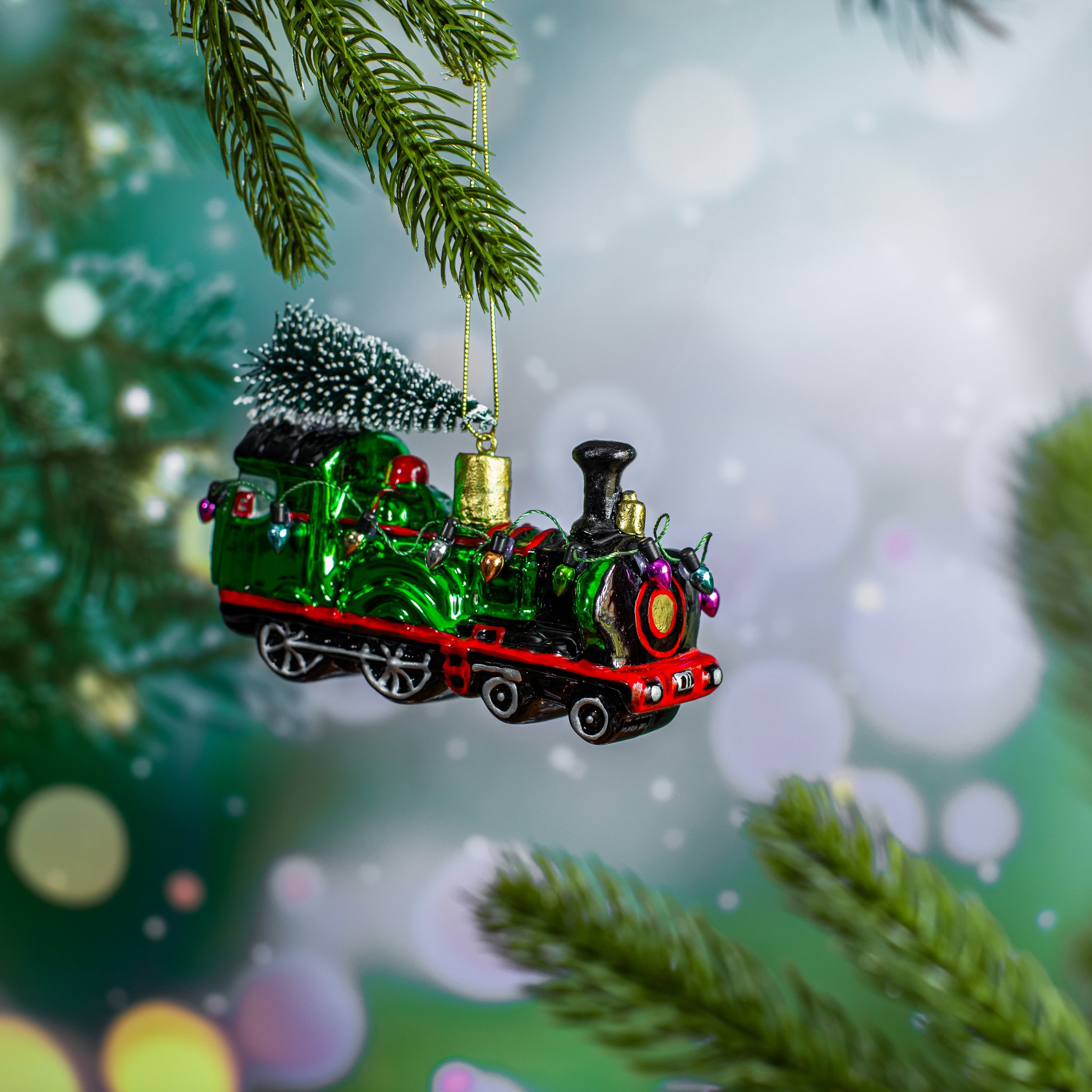 Glass Christmas train hanging from a fir branch against a sparkling background