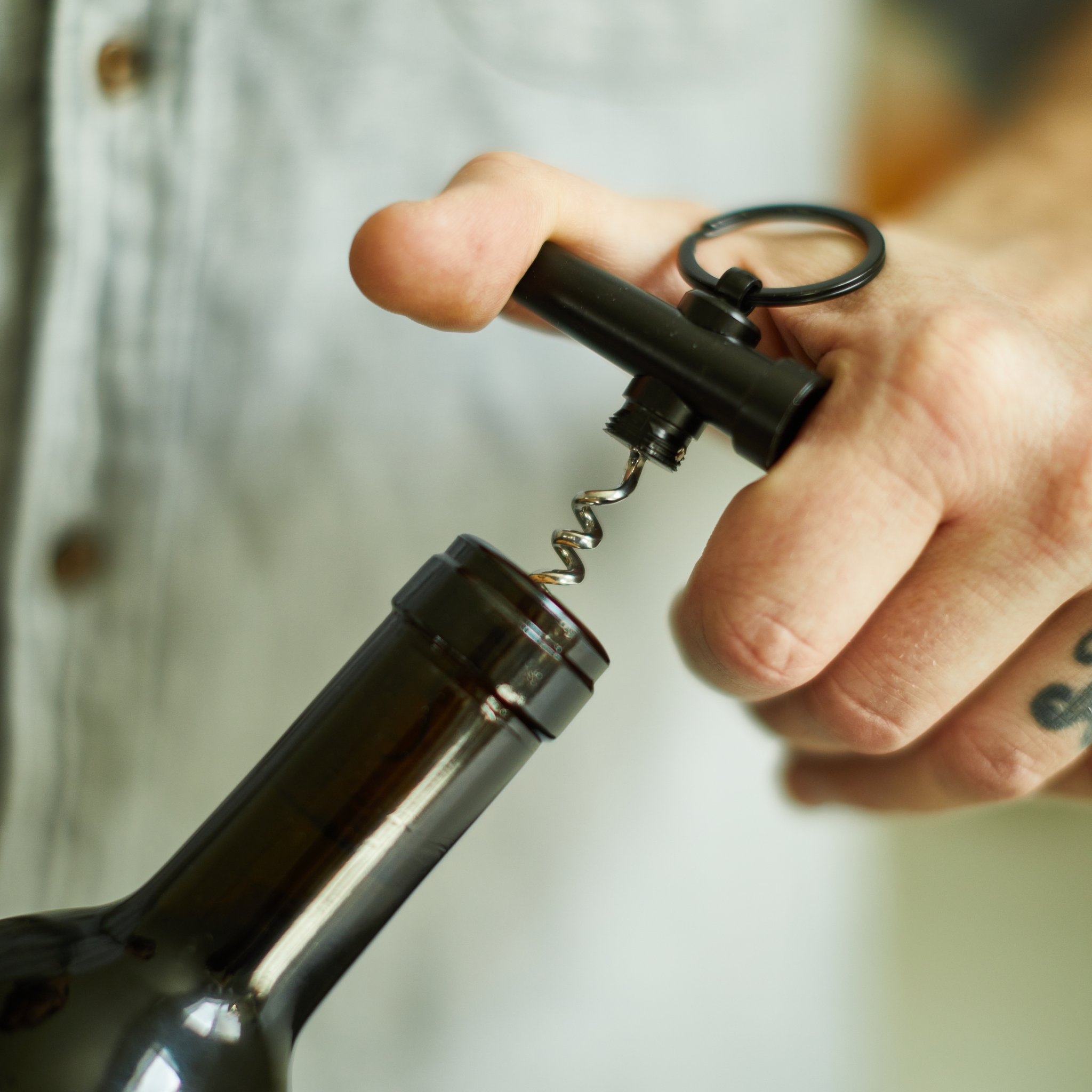 Hand placing the keychain corkscrew onto a dark wine bottle, close-up from the side