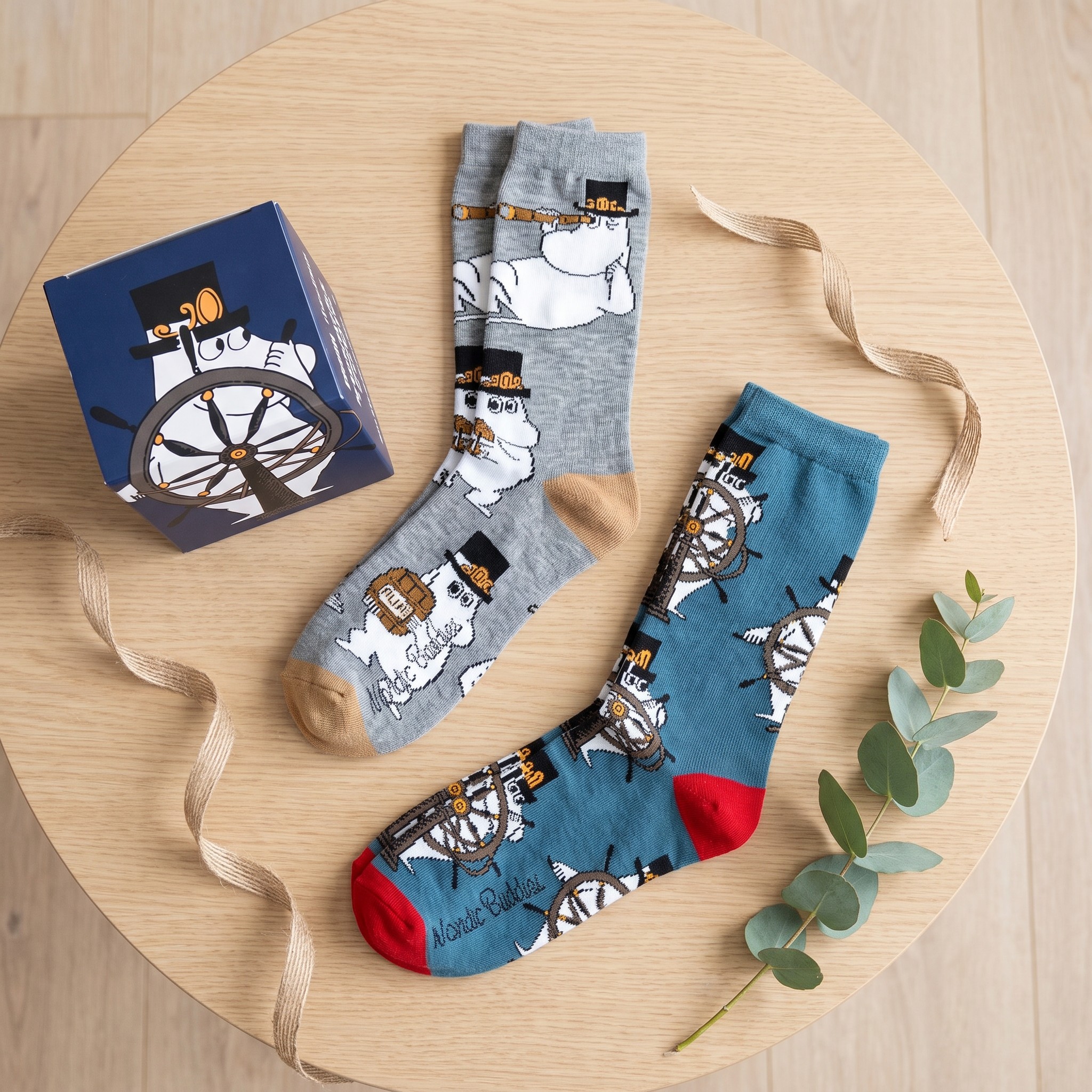 Le due paia di calze Moomin accanto alla scatola regalo blu scuro su un tavolo di legno