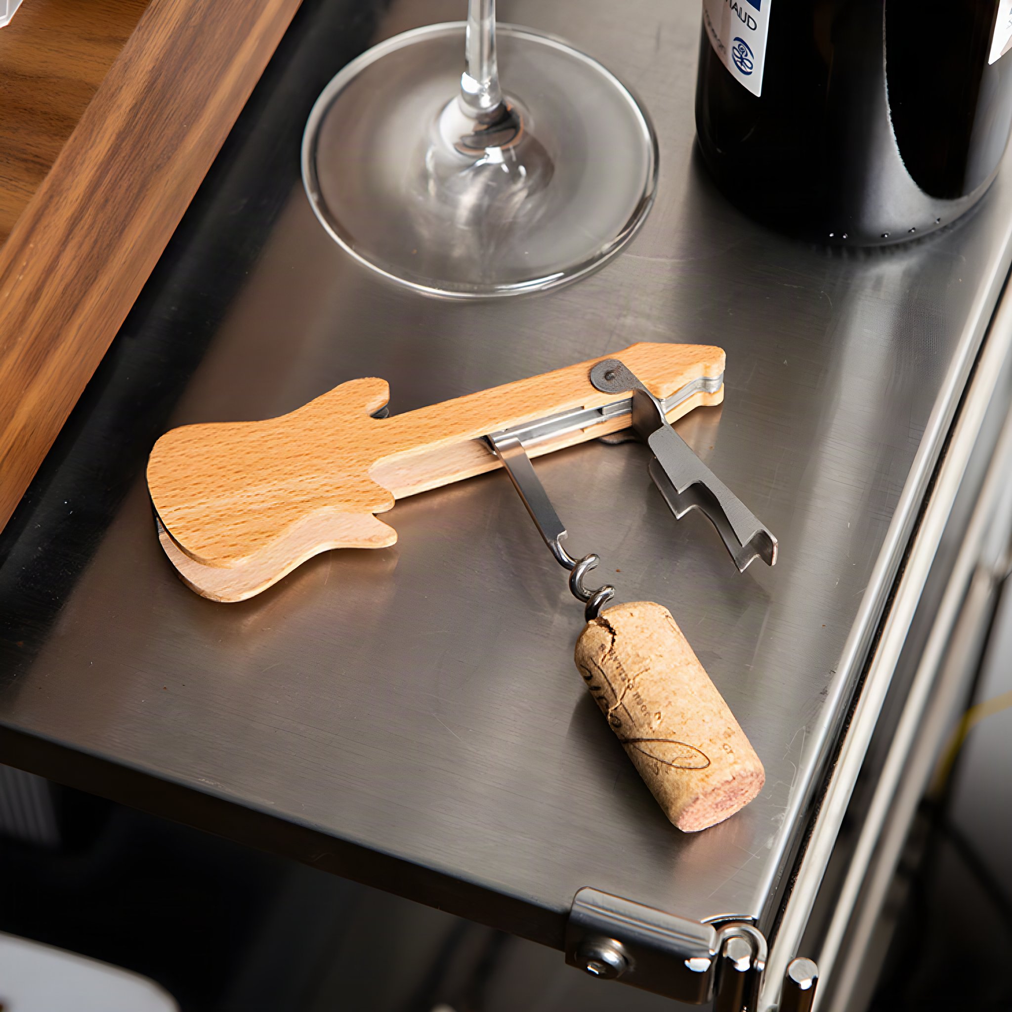 Gitarren-Korkenzieher mit gezogenem Korken neben Weinglas und Flasche