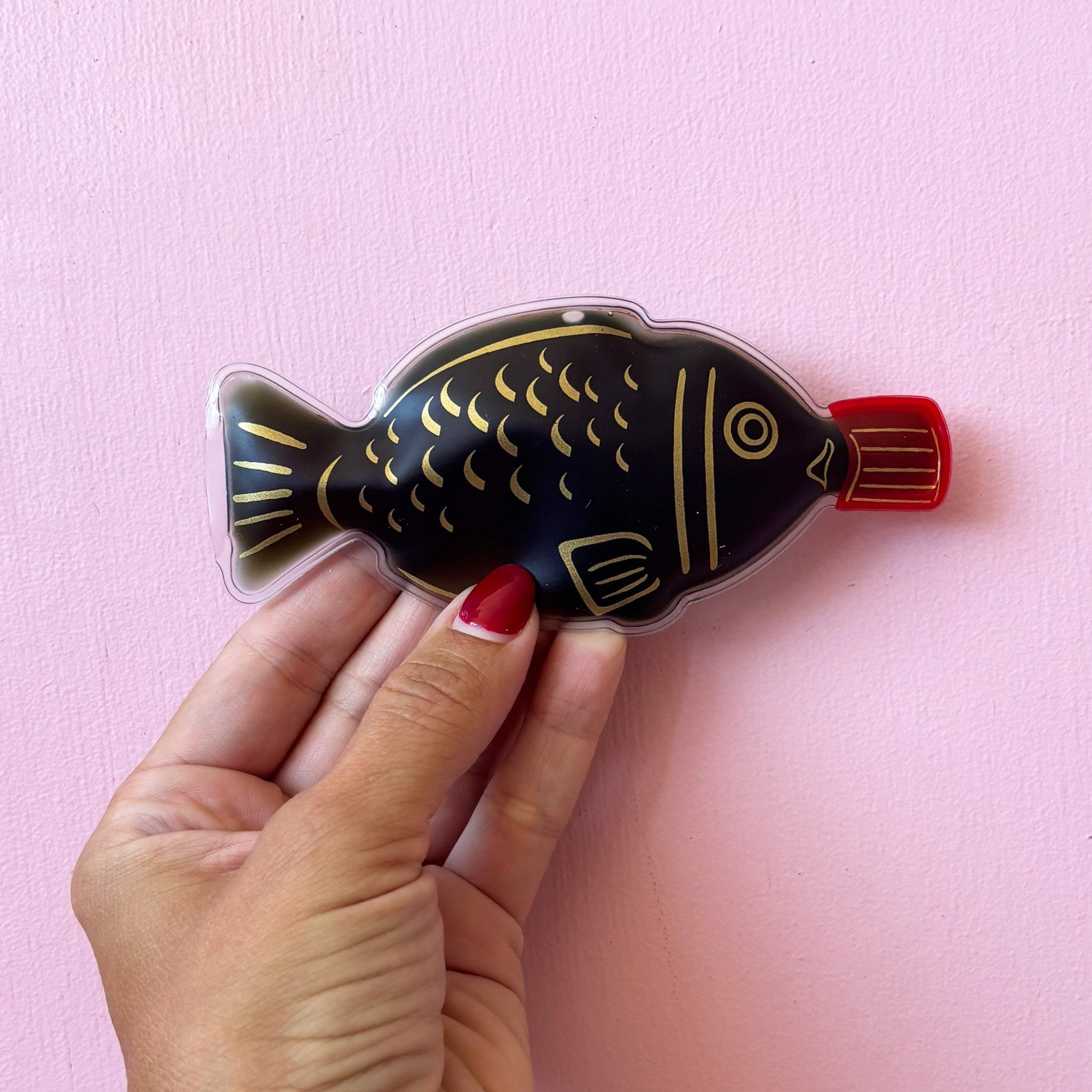 Black fish hand warmer with gold lines against a pink wall
