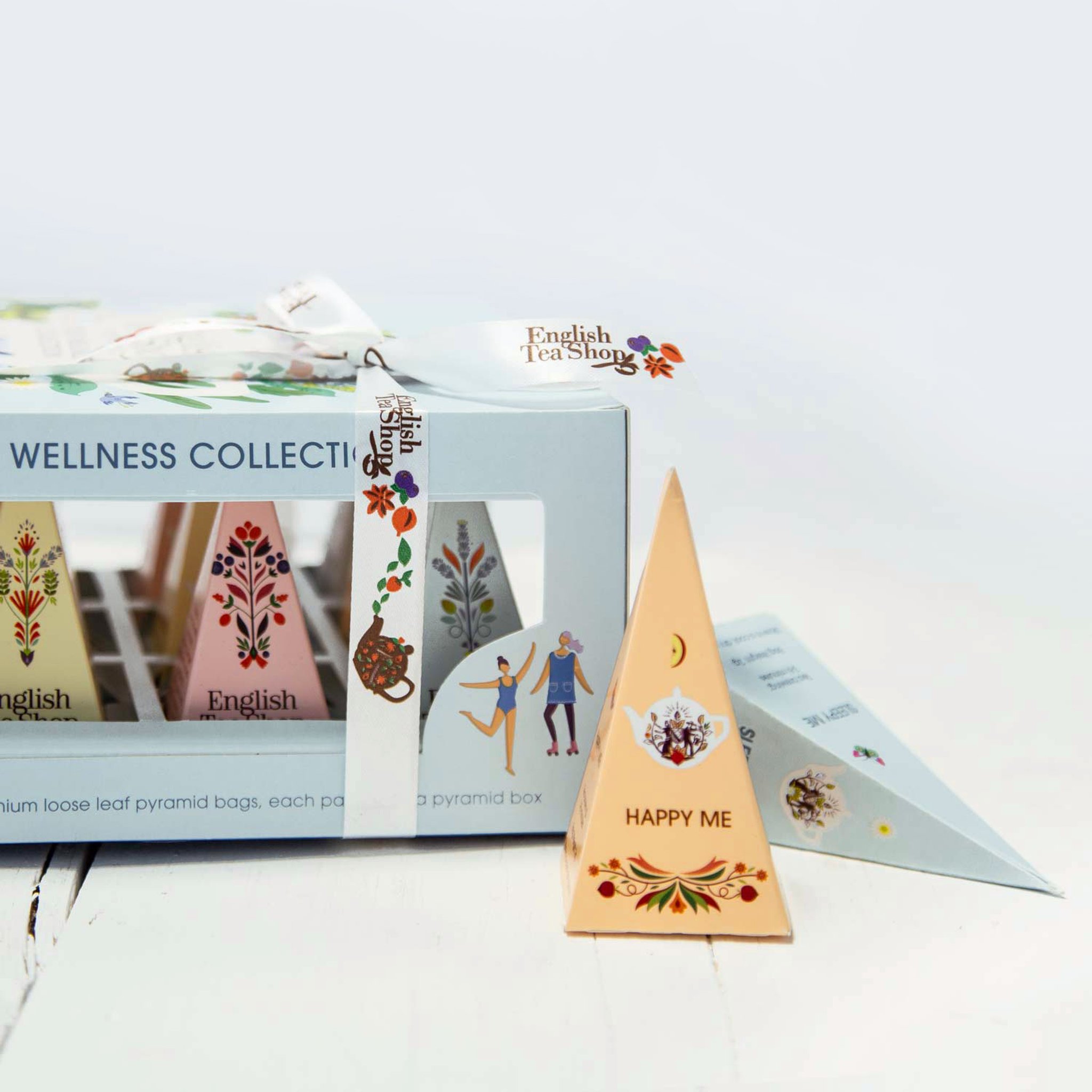 Coffret de thés bien-être sur bois clair, devant une pyramide Happy Me