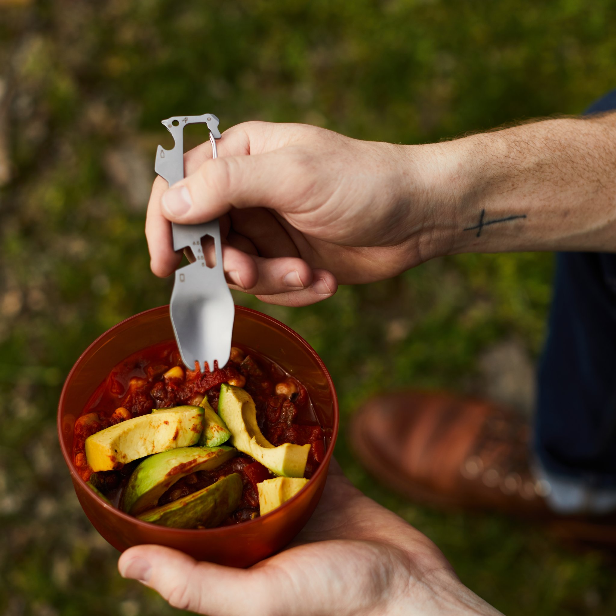 Homme en plein air tenant la fourchette multifonctions au-dessus d'un bol de chili garni d'avocat