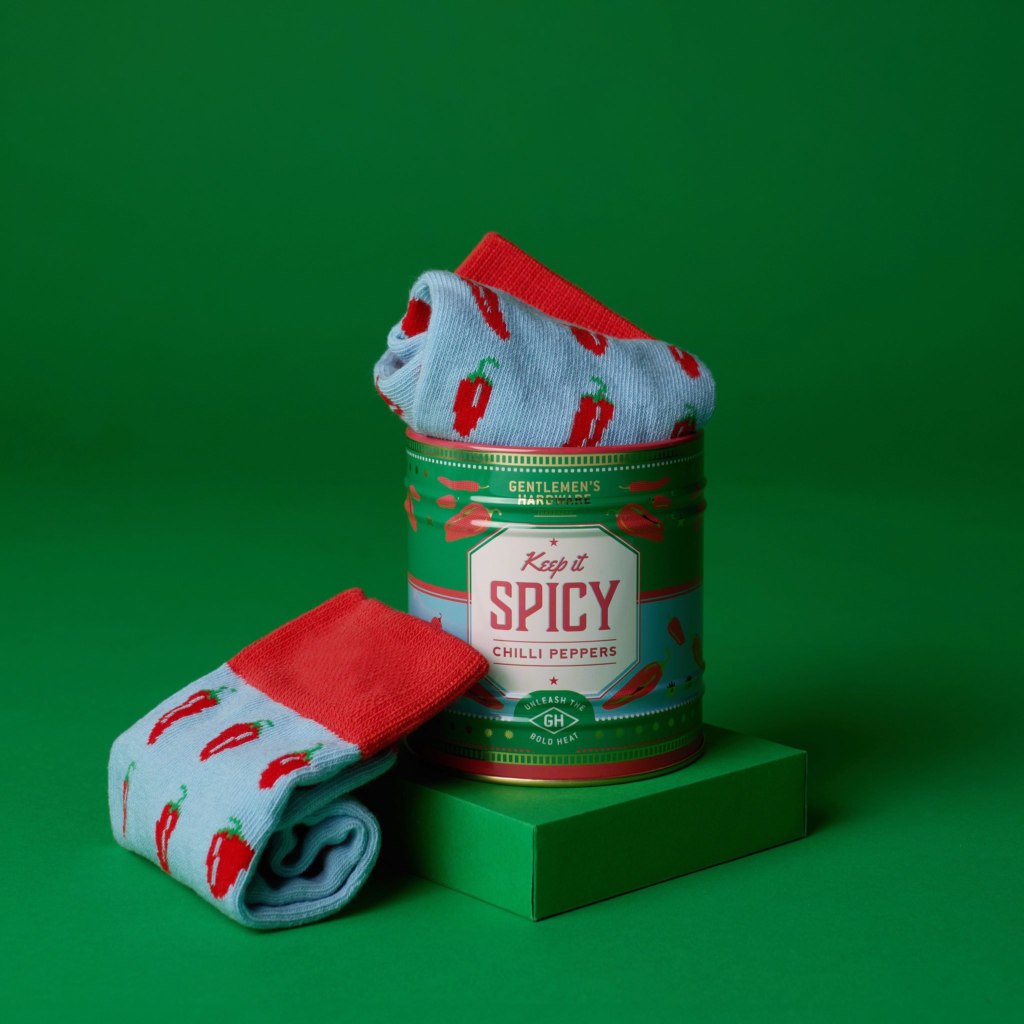Socks in a Can on a green backdrop: the tin with a folded sock on top stands on a block, a second sock beside it