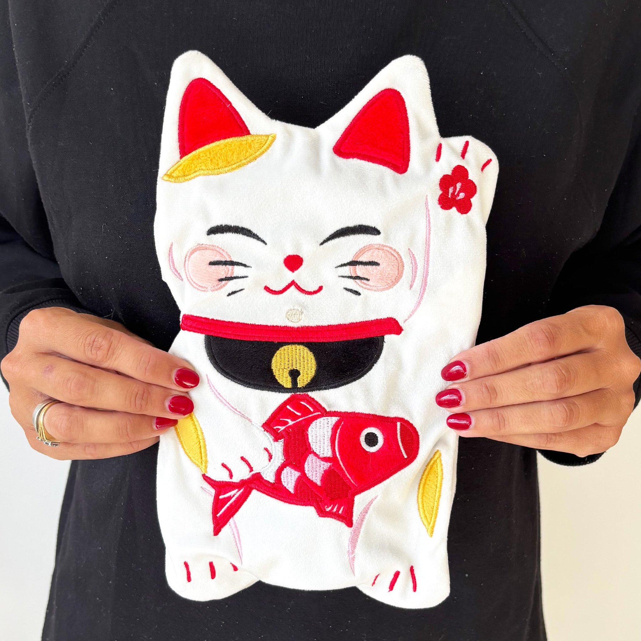 Lucky cat hot water bottle with red fish, held in front of the body