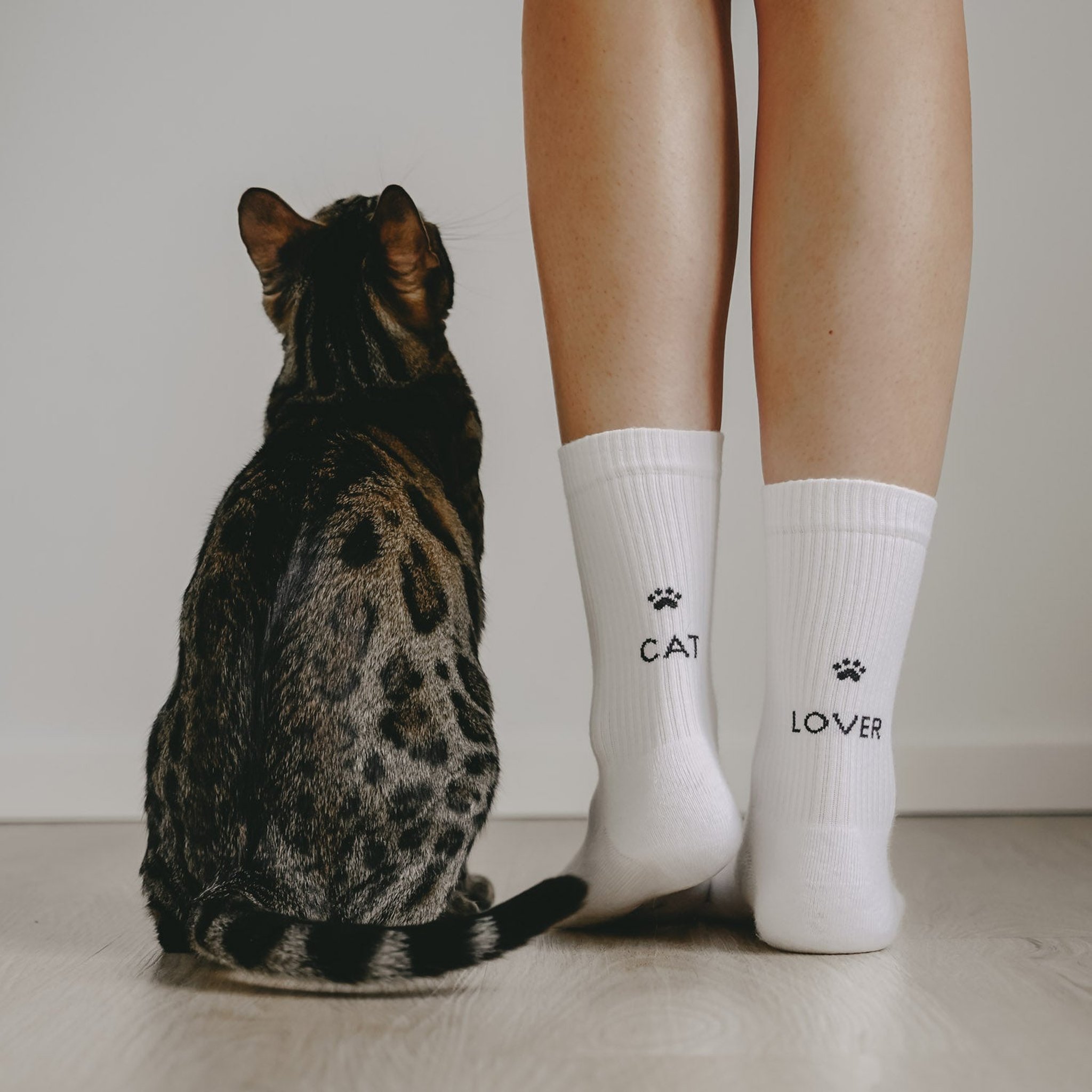 Gefleckte Katze sitzt neben Beinen in den weissen Socken Cat Lover