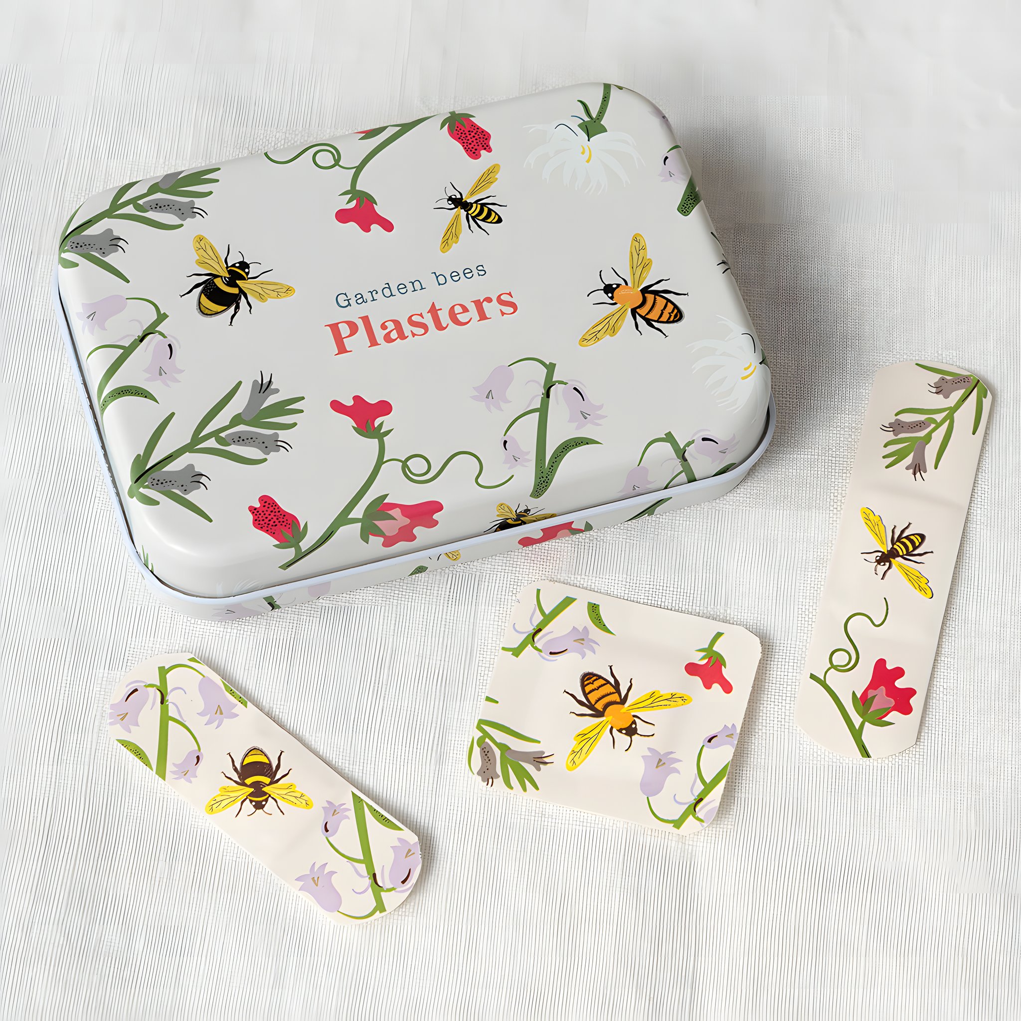 Dose mit Bienen-Pflastern auf hellem Leinen, daneben drei Pflaster mit Bienen und Blumen