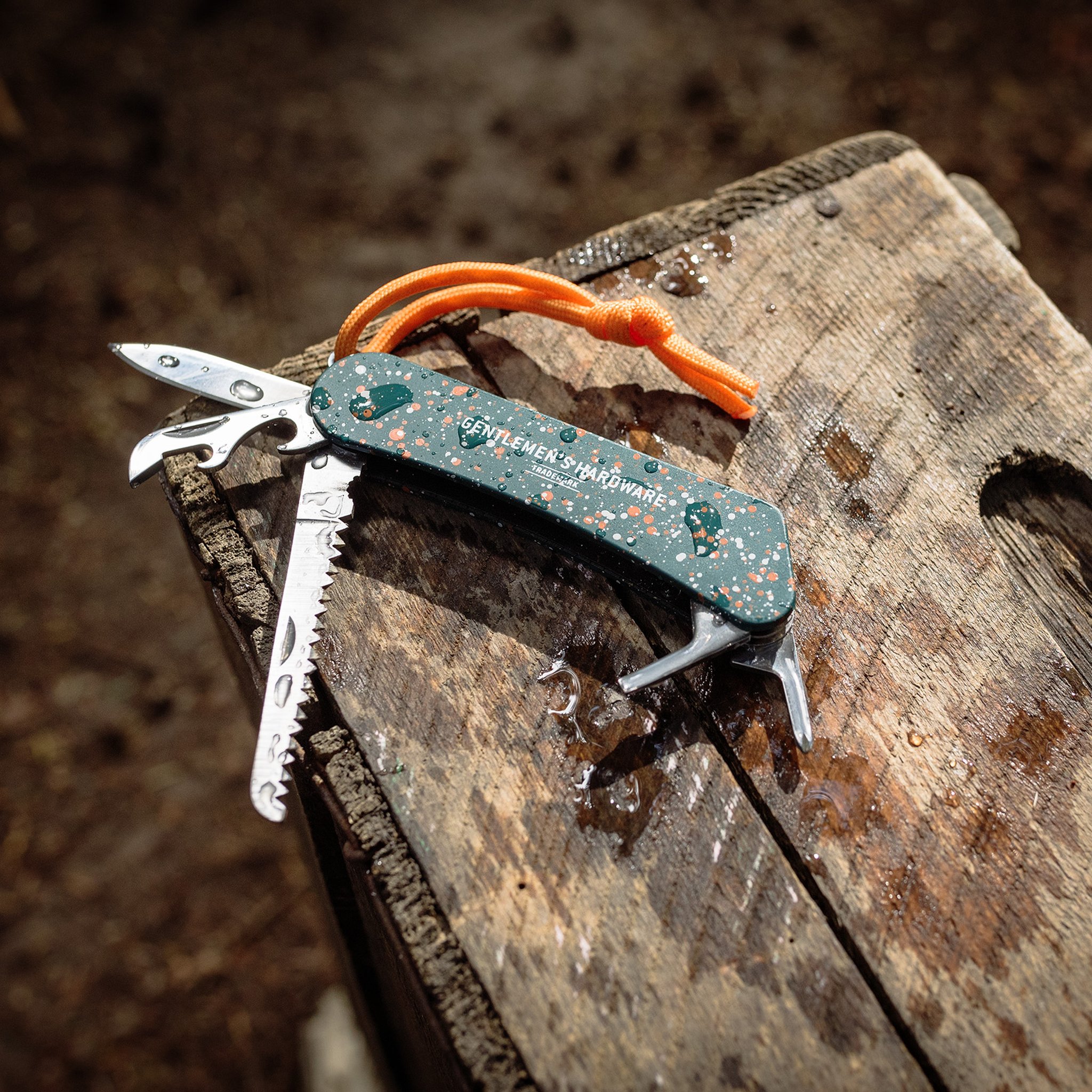 Nasses grünes Wildnis Multitool mit Säge und Flaschenöffner auf einem verwitterten Holzbrett im Freien