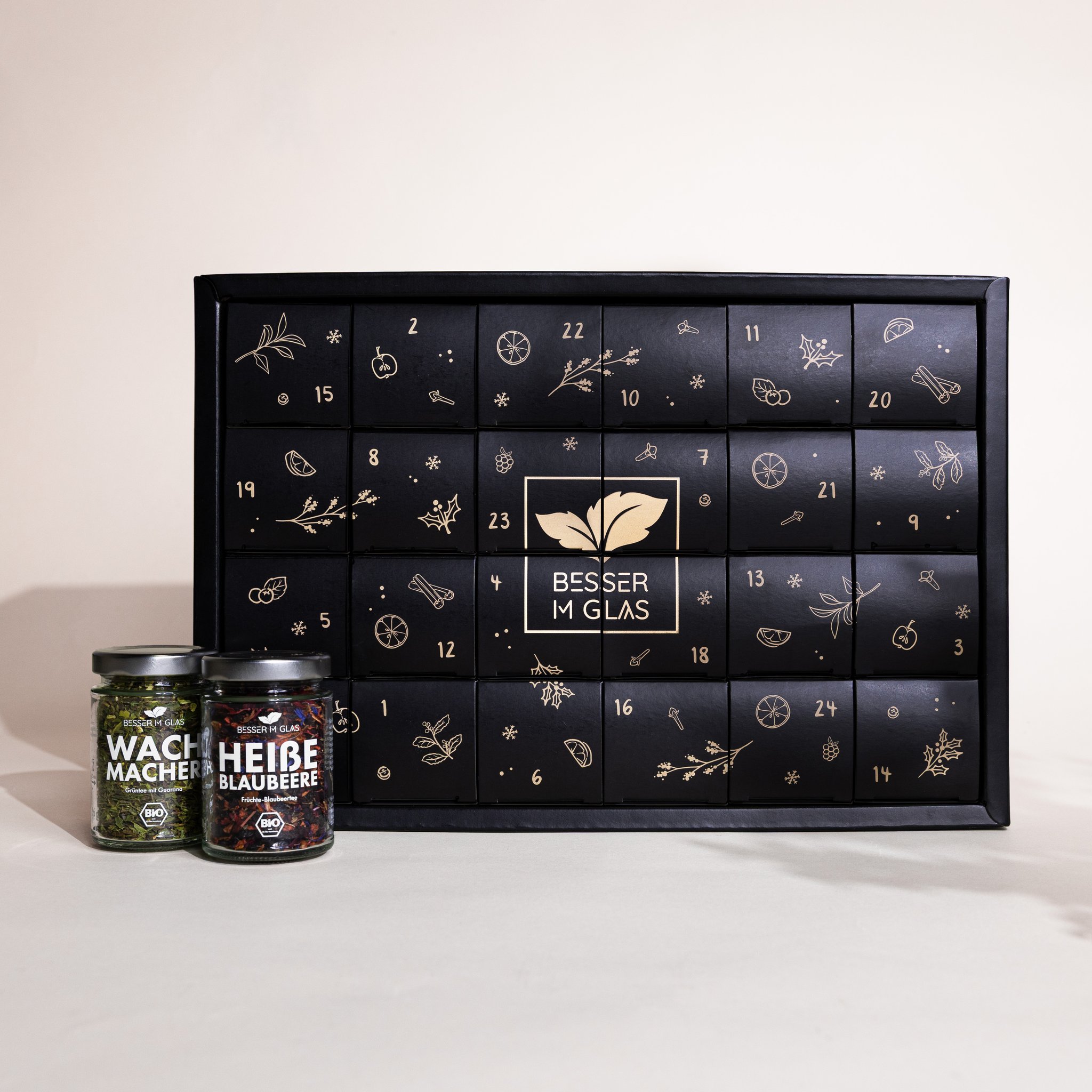Schwarzer Bio Tee-Adventskalender von Besser im Glas mit 24 Türchen, daneben zwei Teegläser