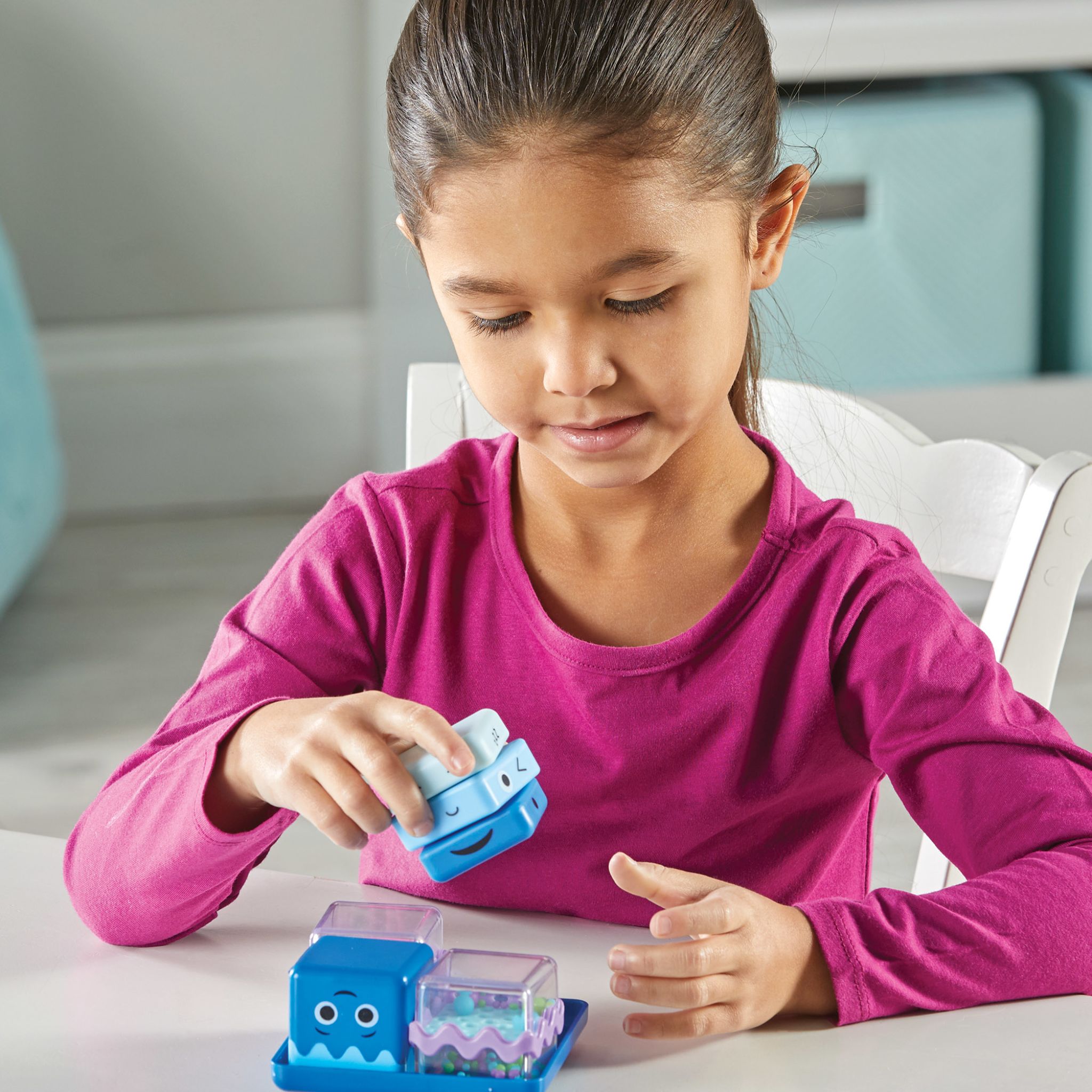 Mädchen spielt am Tisch mit einem Cool Down Cube, die übrigen Würfel liegen im Tablett