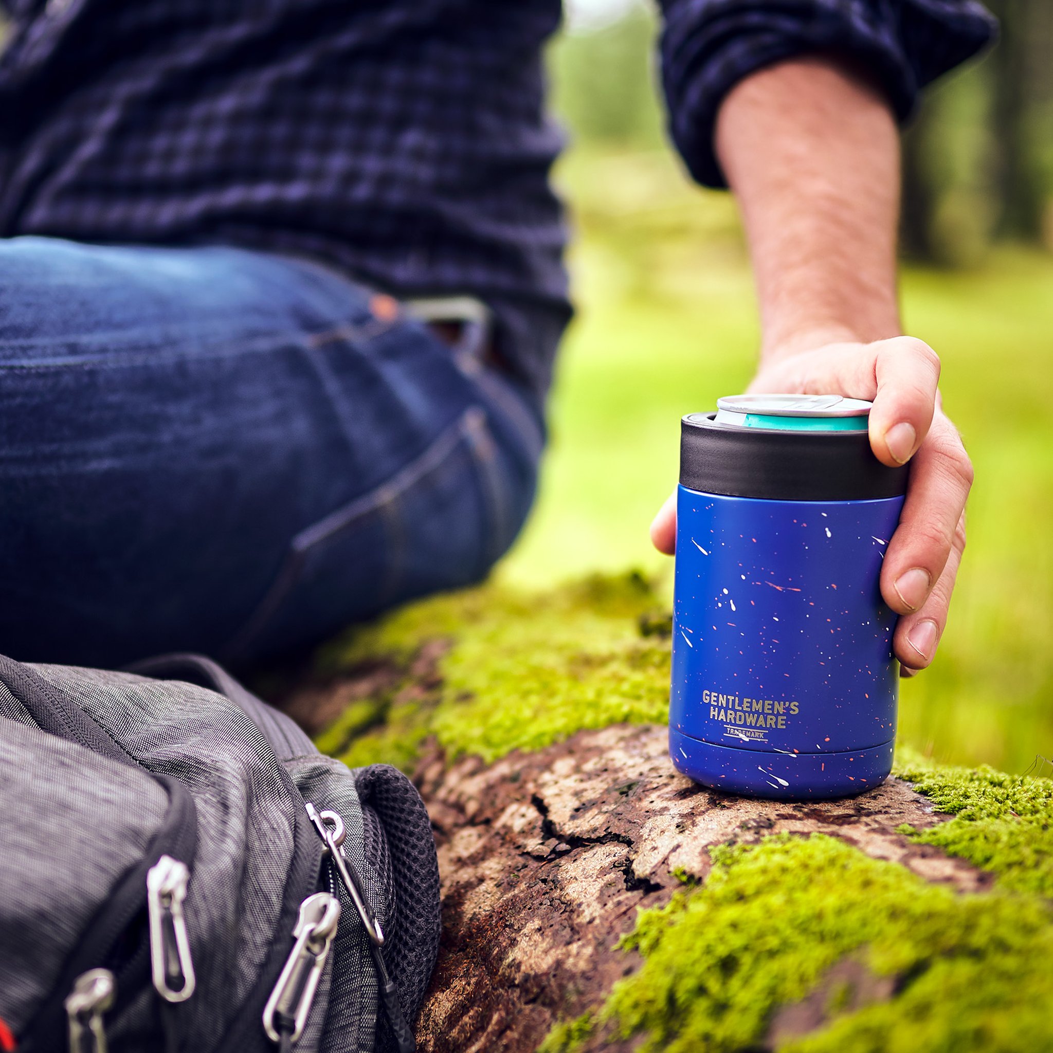 Hand holding the Beverage Cooler on a mossy log in the woods, with a backpack beside it