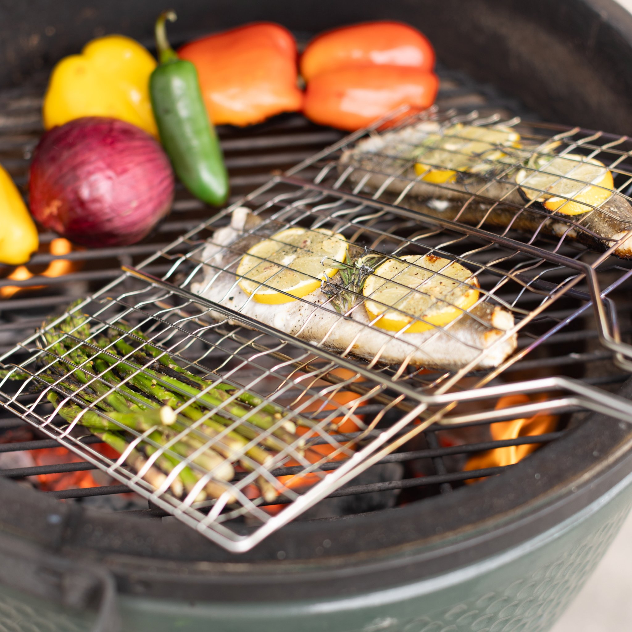 Due cestini per barbecue su una griglia tonda con trota, fette di limone e asparagi verdi, peperoni accanto