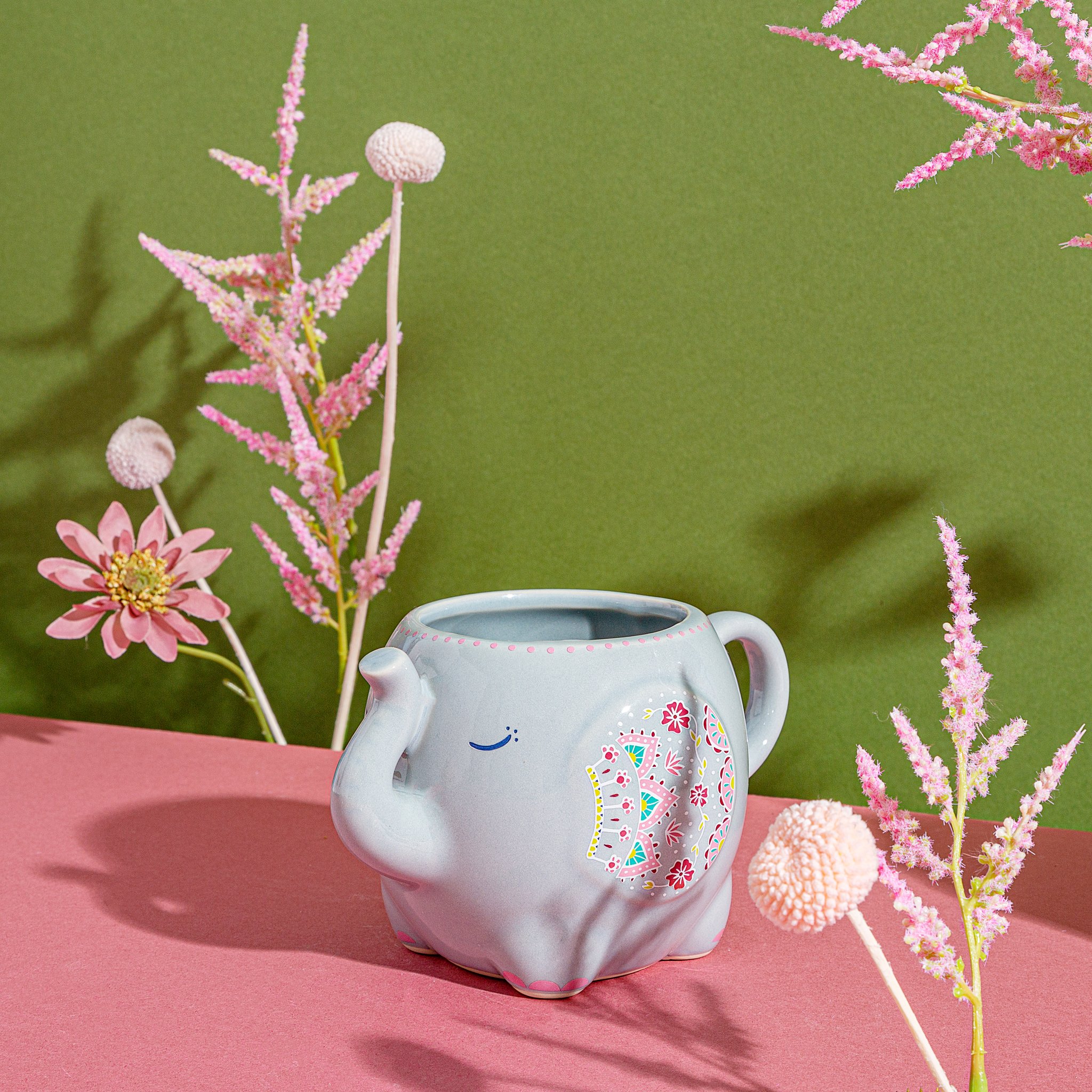 Sass & Belle Mandala Tasse Elefant aus grauer Keramik mit buntem Mandala-Motiv, Lifestyle vor grüner Wand mit pinken Astilbe-Blüten