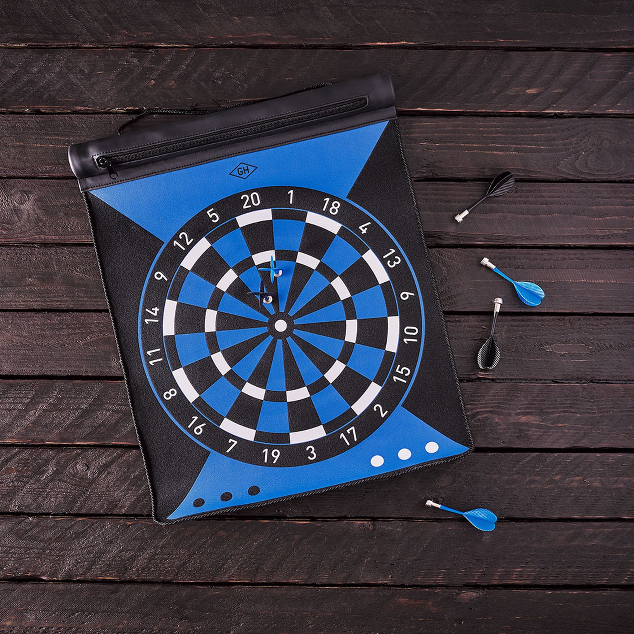 Roll-Up Dartscheibe auf dunklem Holztisch, zwei Darts stecken im Board, weitere Darts liegen daneben