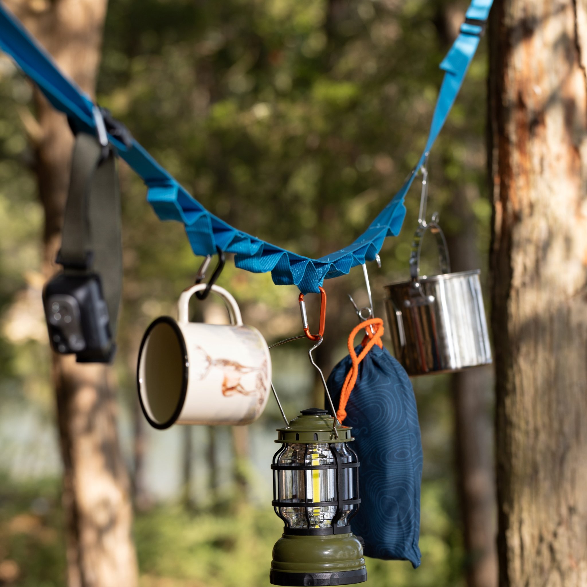 Enamel mug with a stag motif and a headtorch hanging from the Hanging tent tidy against a blurred forest