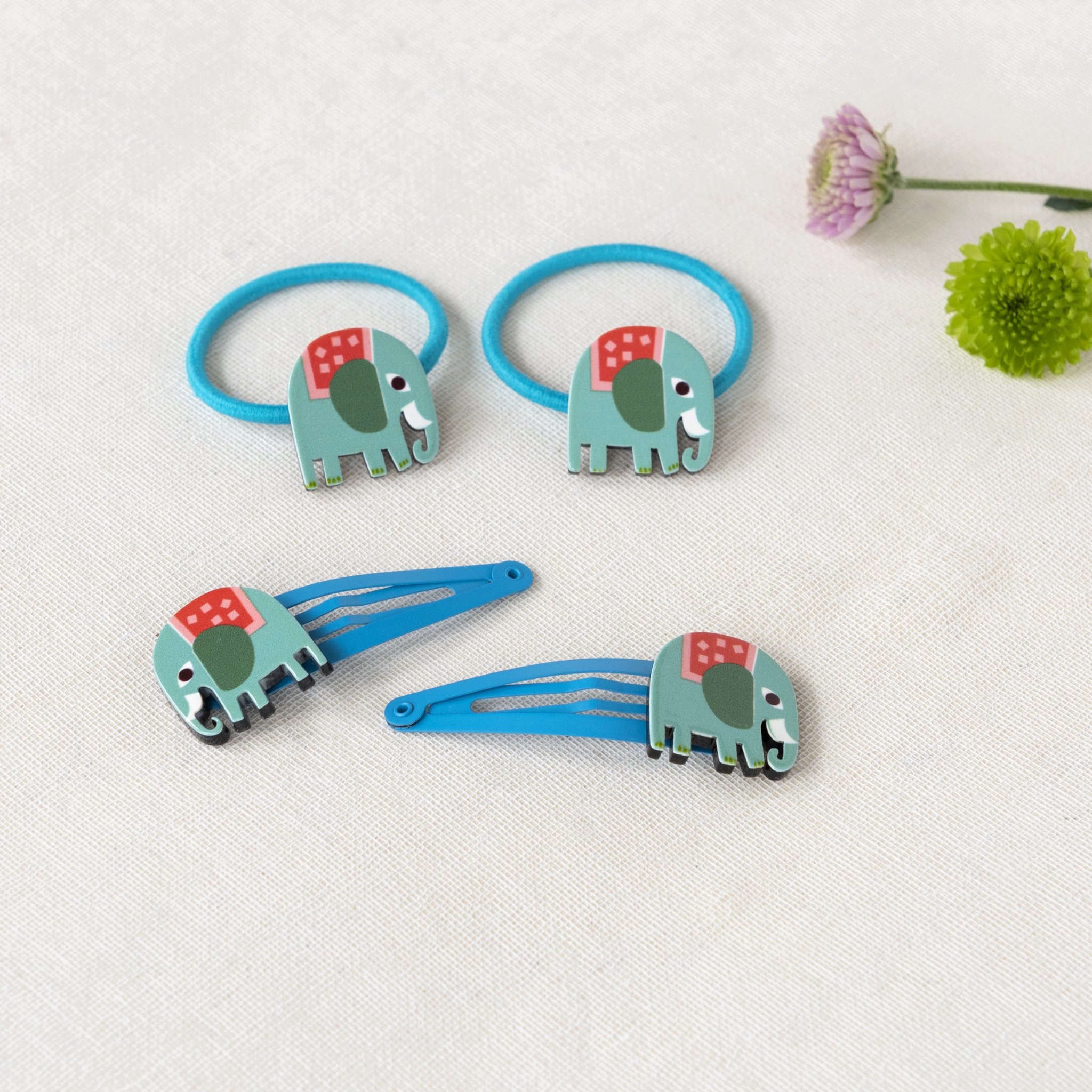 Elephant hair clips and matching hair ties on linen next to a blossom