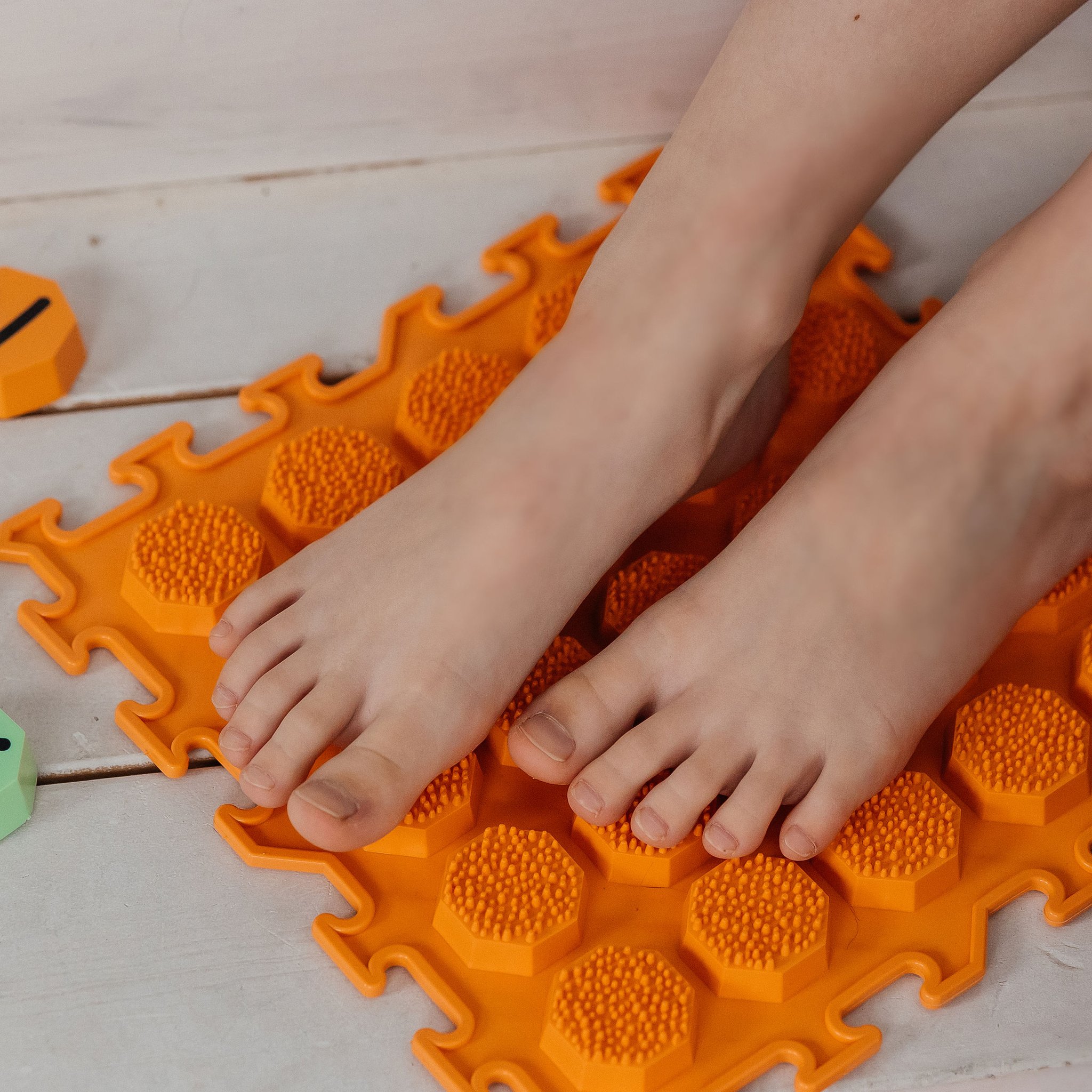 Barfuss auf der orangen Noppenmatte des Sensorikmatten-Sets, daneben Zahlen-Achtecke