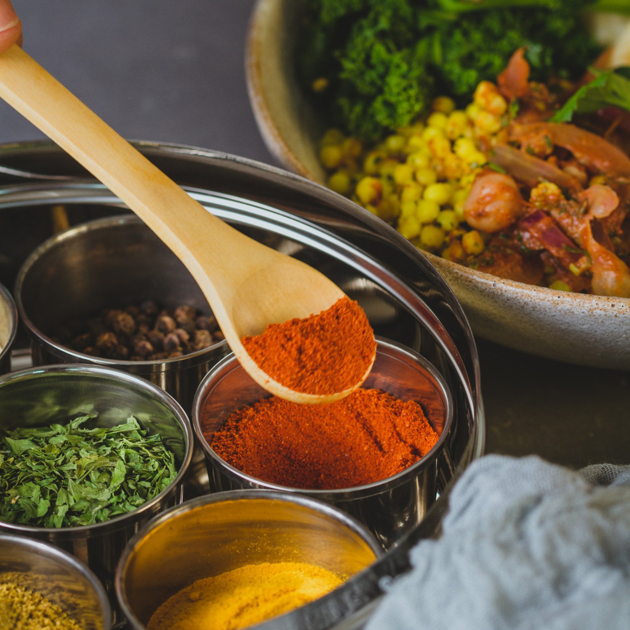 Holzlöffel mit Paprikapulver über Masala Dabba, Curry-Schüssel daneben