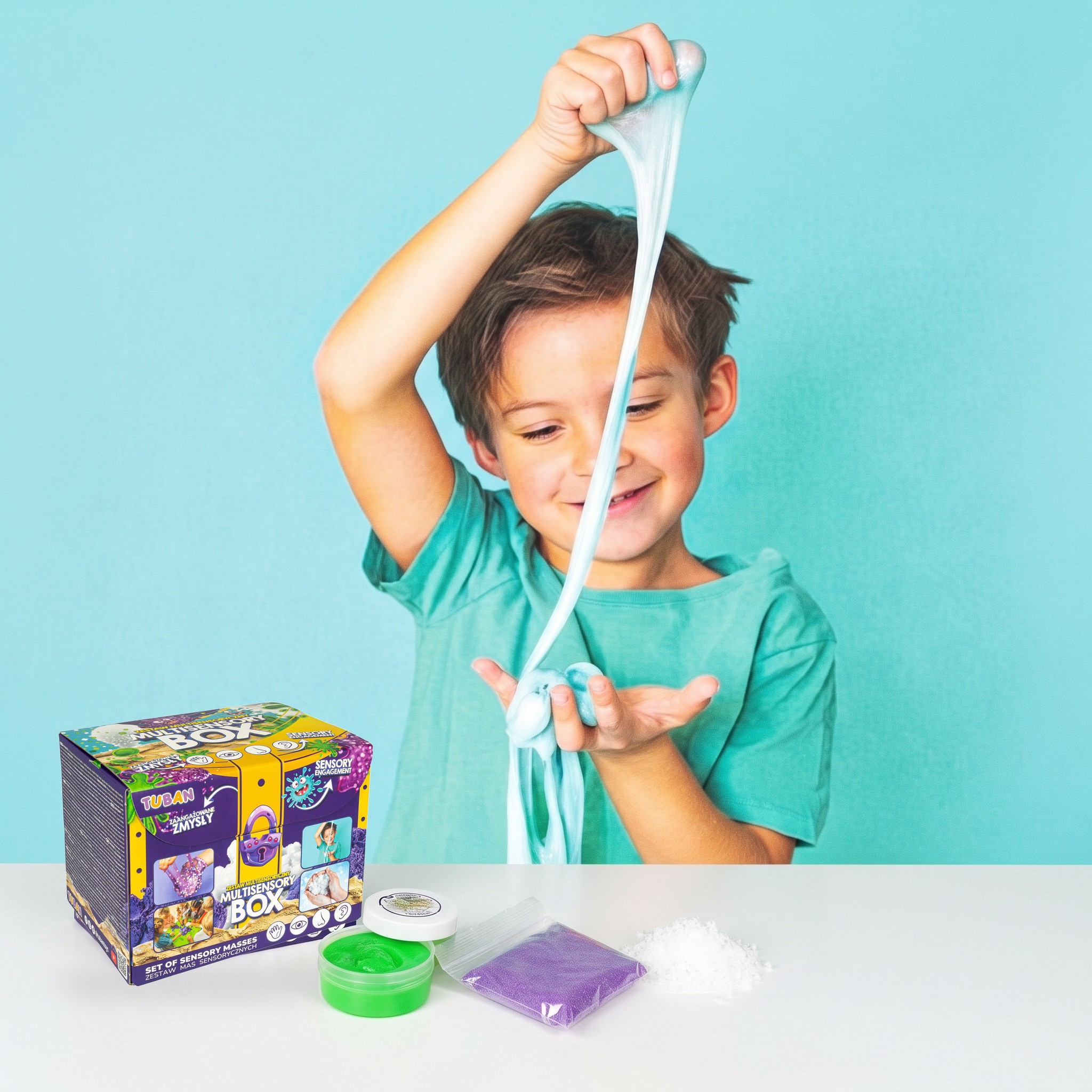 Bambino che allunga lo slime azzurro, davanti la scatola multisensoriale con slime verde, sabbia dinamica viola e neve artificiale