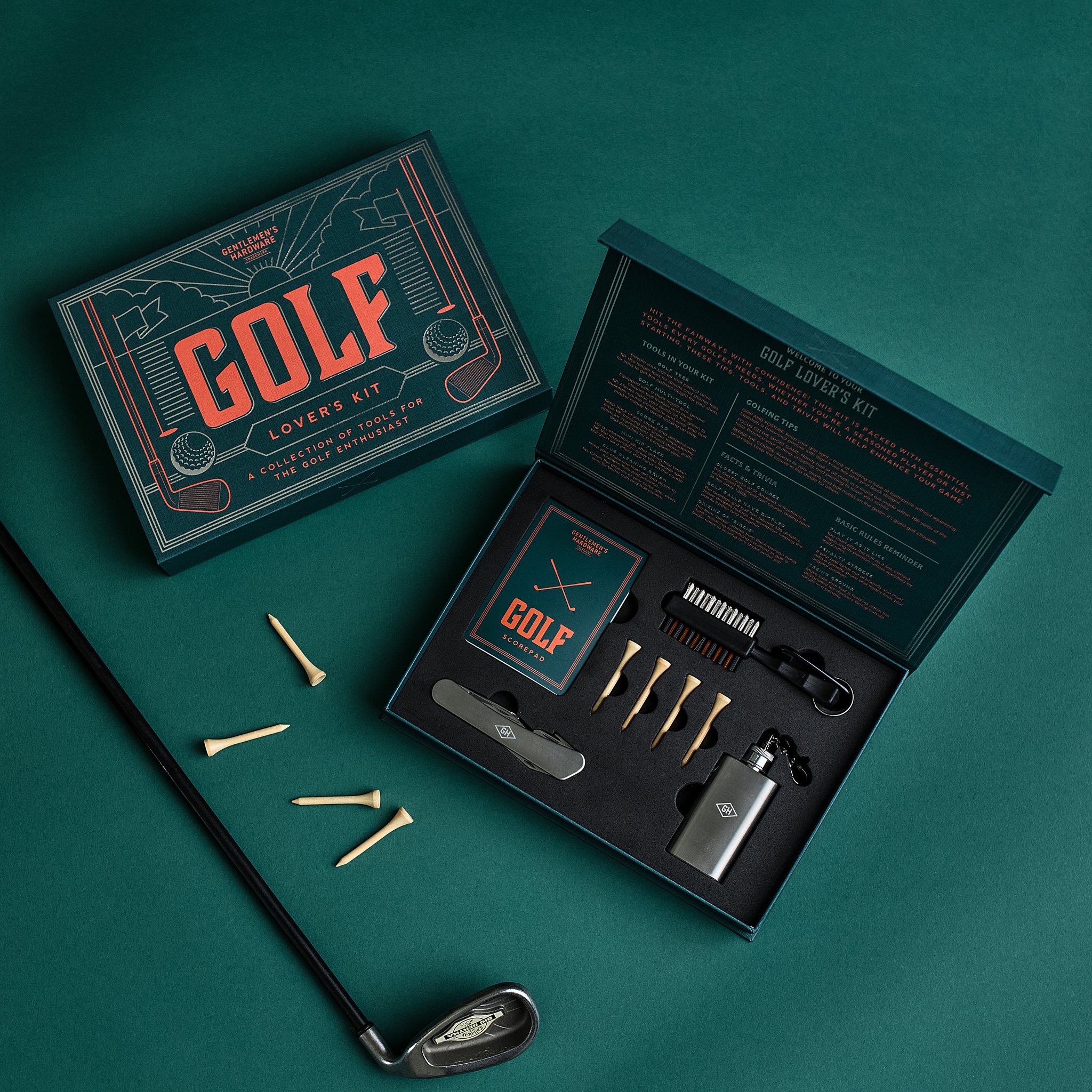 Golf Liebhaber Set offen und geschlossen auf grünem Untergrund, daneben ein Eisen und verstreute Holz-Tees