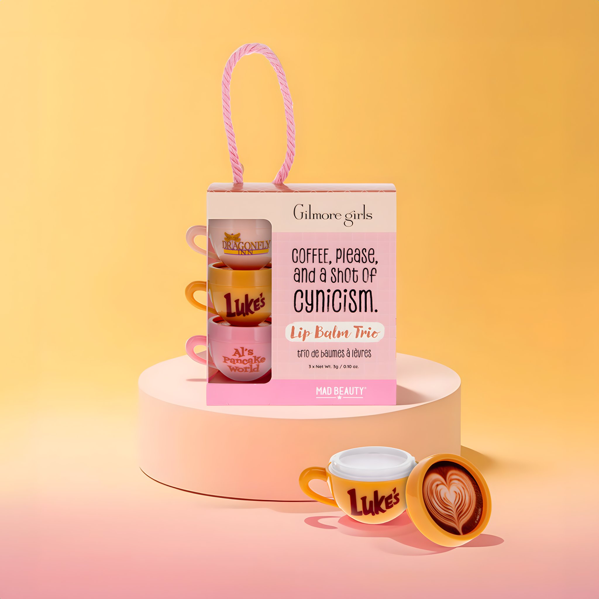 Gilmore Girls Lippenbalsam-Trio in Geschenkschachtel auf rosa Podest mit geöffneter Luke's-Tasse