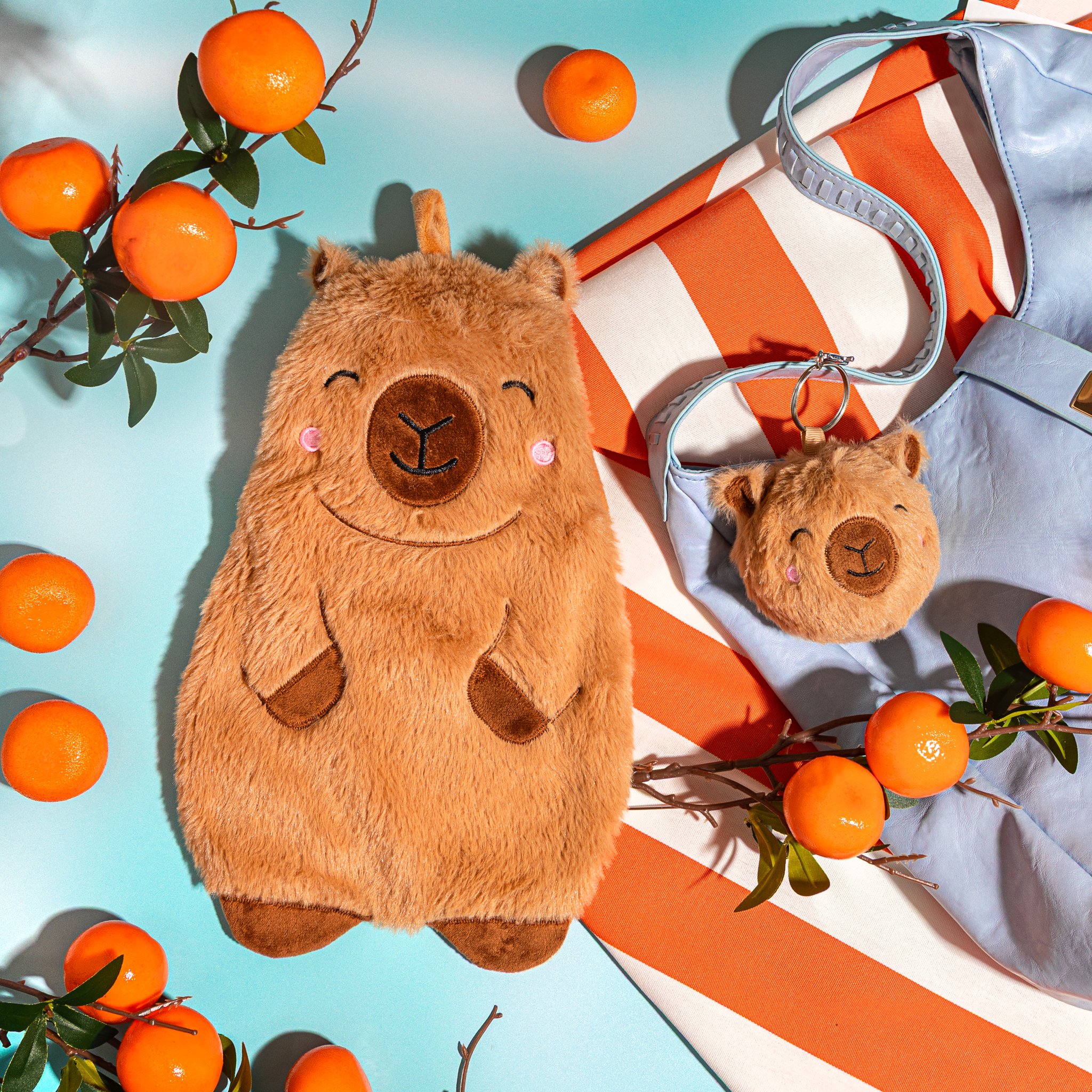 Bouillotte capybara Sass & Belle avec mandarines et porte-clés capybara sur un tissu bleu