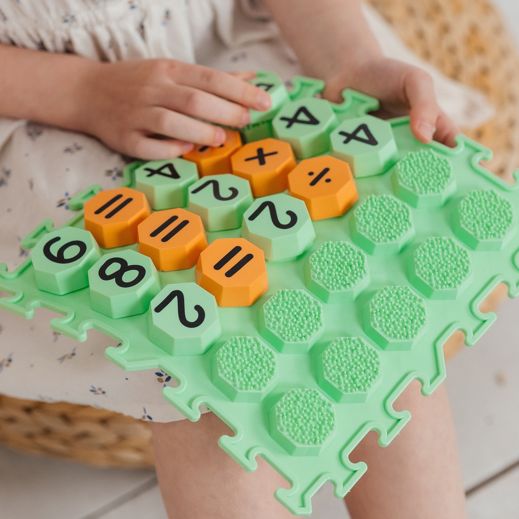 Kinderhand setzt ein oranges Zahlen-Achteck in die Vertiefung der Sensorikmatte