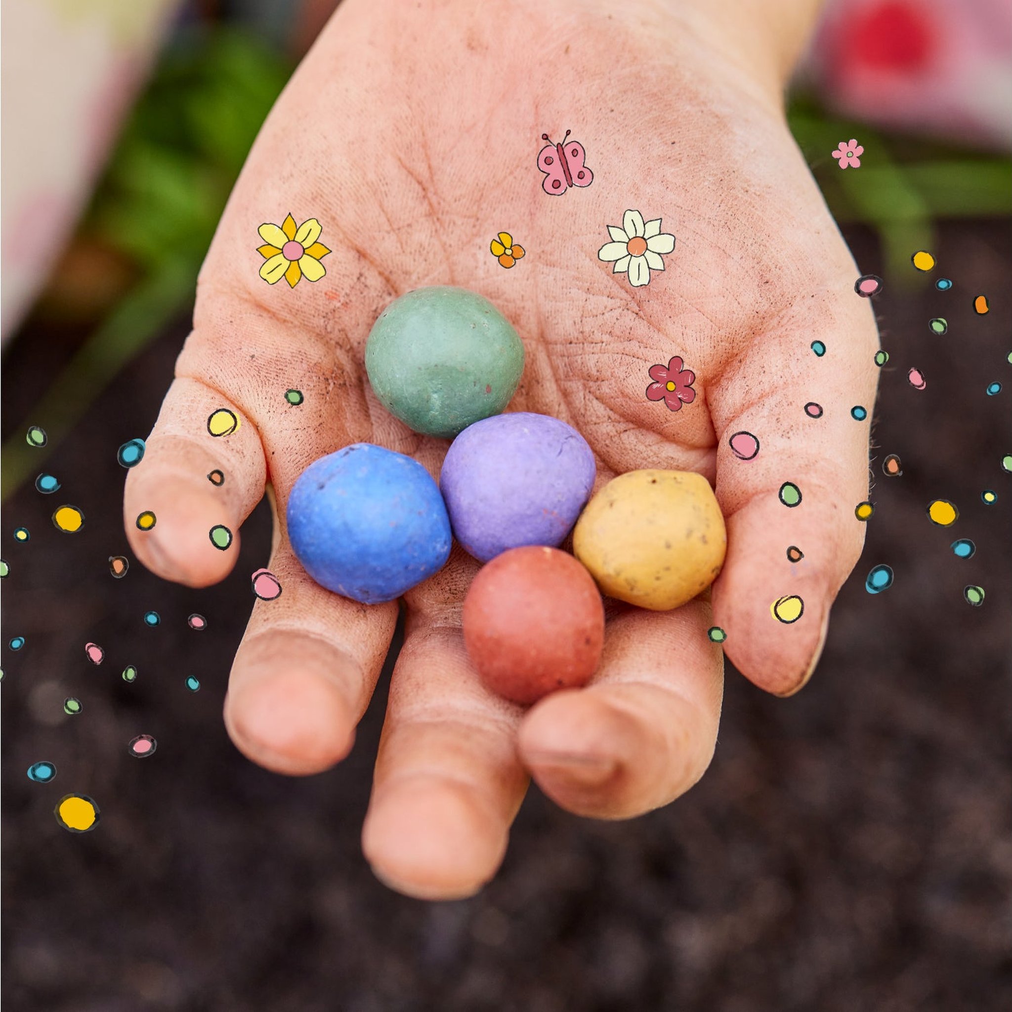 Offene Hand mit fünf bunten Blumenmurmeln über Gartenerde