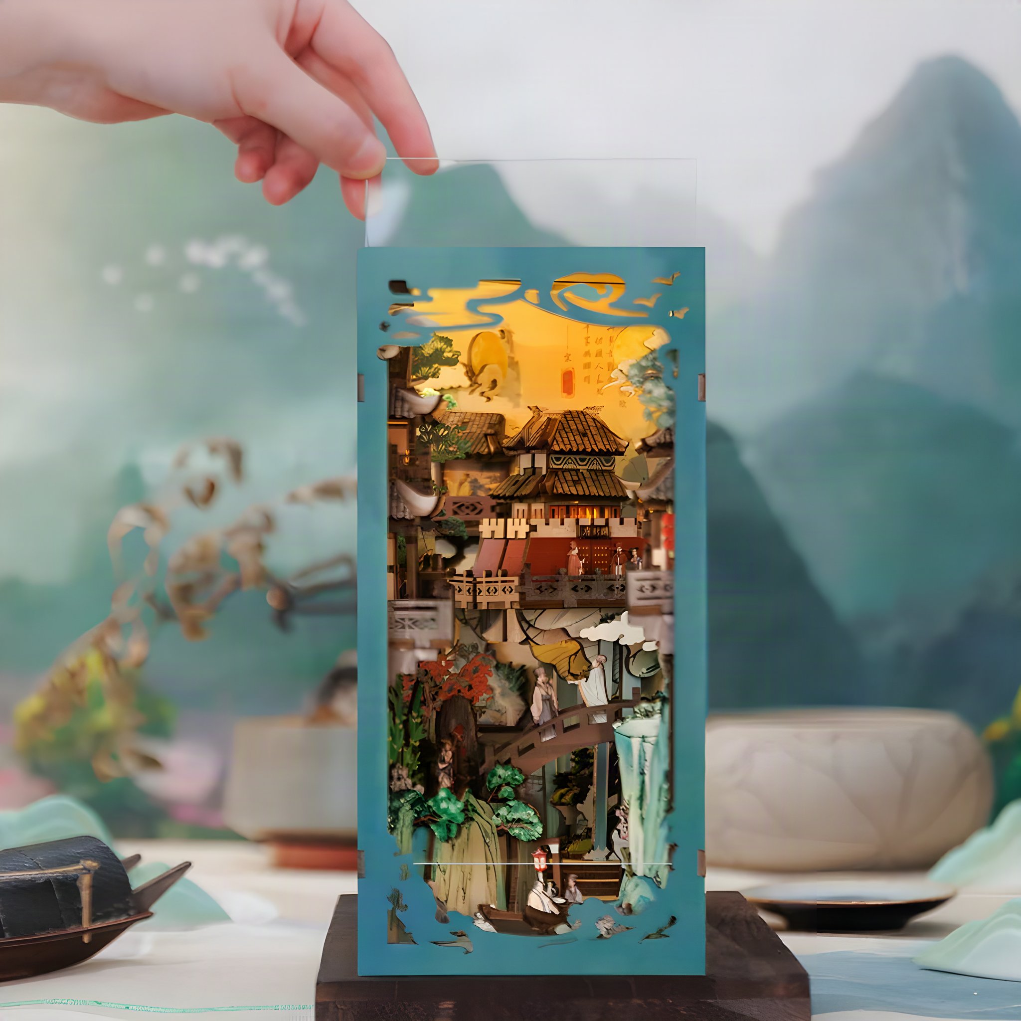 Une main pose la fine scène miniature avec pavillons et cascade