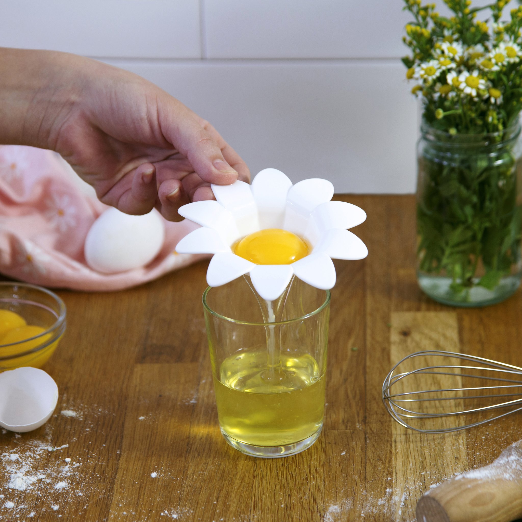 Hände trennen ein Ei mit dem Gänseblümchen Eitrenner über einem Glas