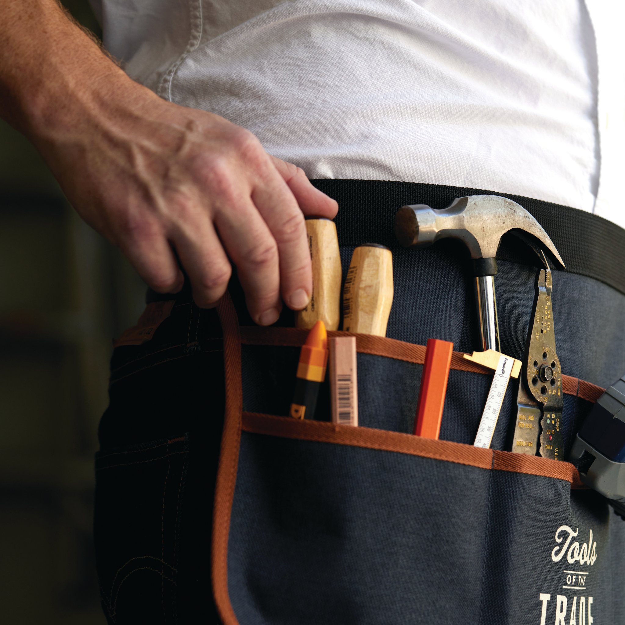 Man in a white shirt wearing the Tool Belt, its pockets holding a hammer, screwdrivers, pliers and a folding rule