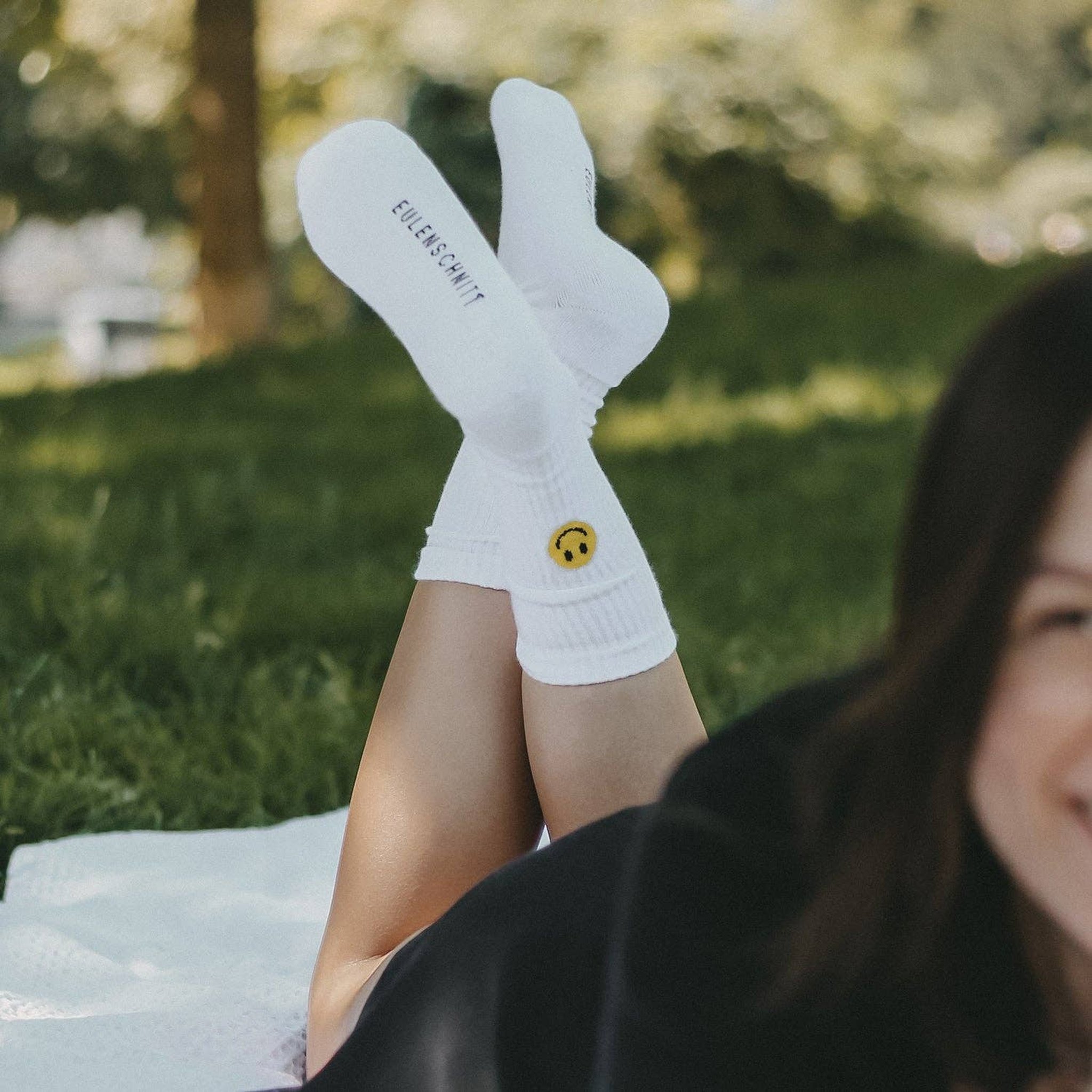 Frau liegt auf einer Wiese und streckt die Füsse in den Smiley-Socken in die Luft