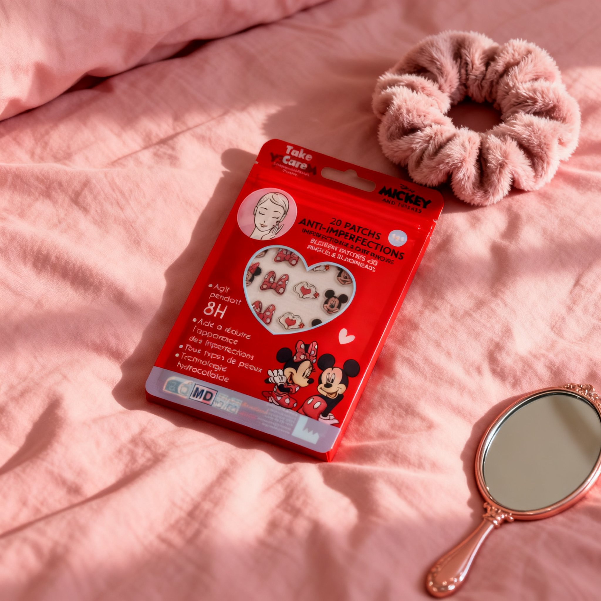 Pouch of Minnie blemish patches lying flat on pink bedding, with a scrunchie beside it