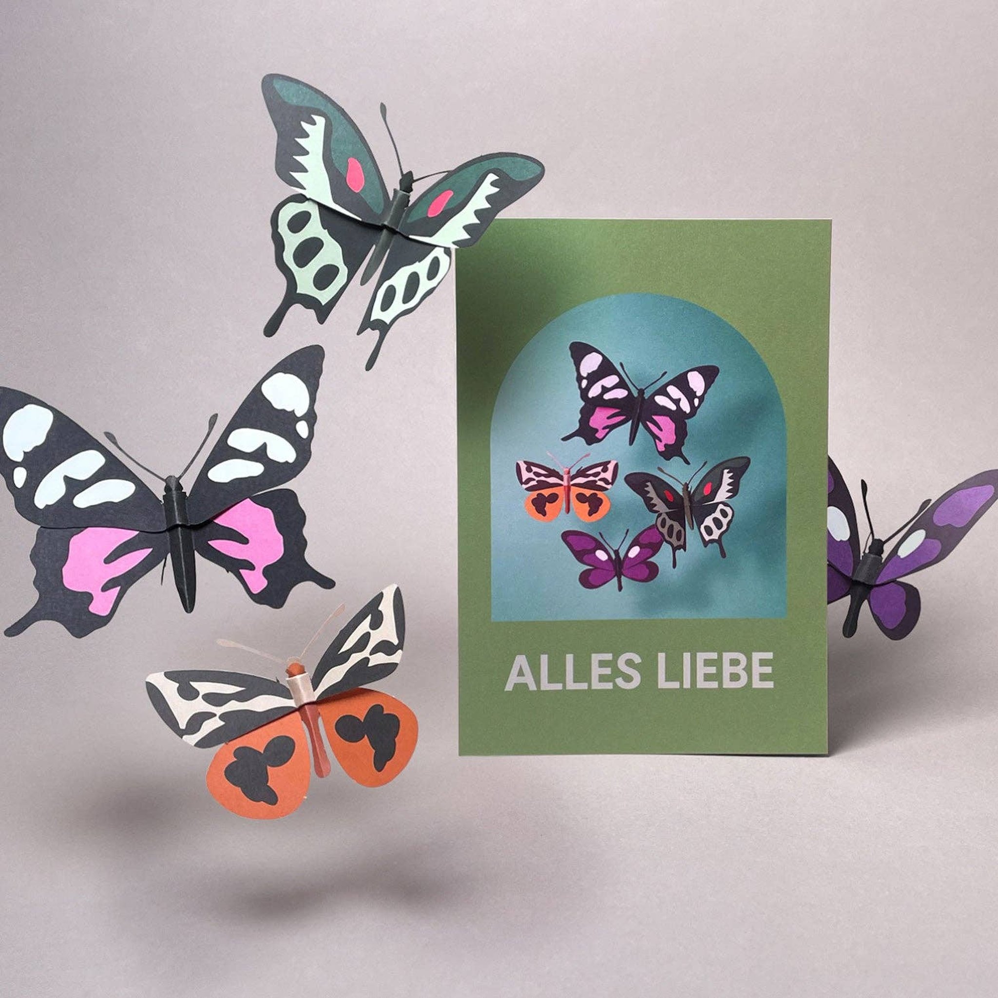 Gefaltetes 3D-Modell Schmetterlinge neben der Grusskarte «Alles Liebe» von Faltmeister