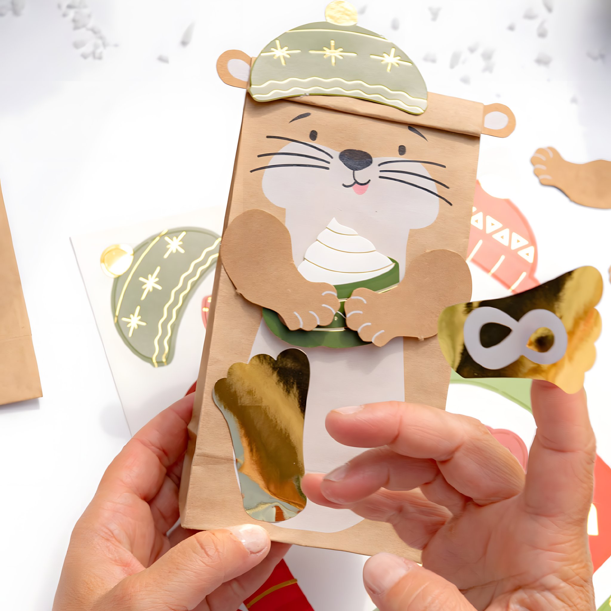 Hände setzen Stanzteile mit Goldfolie auf eine Kraftpapiertüte des Otterfamilie Adventskalenders