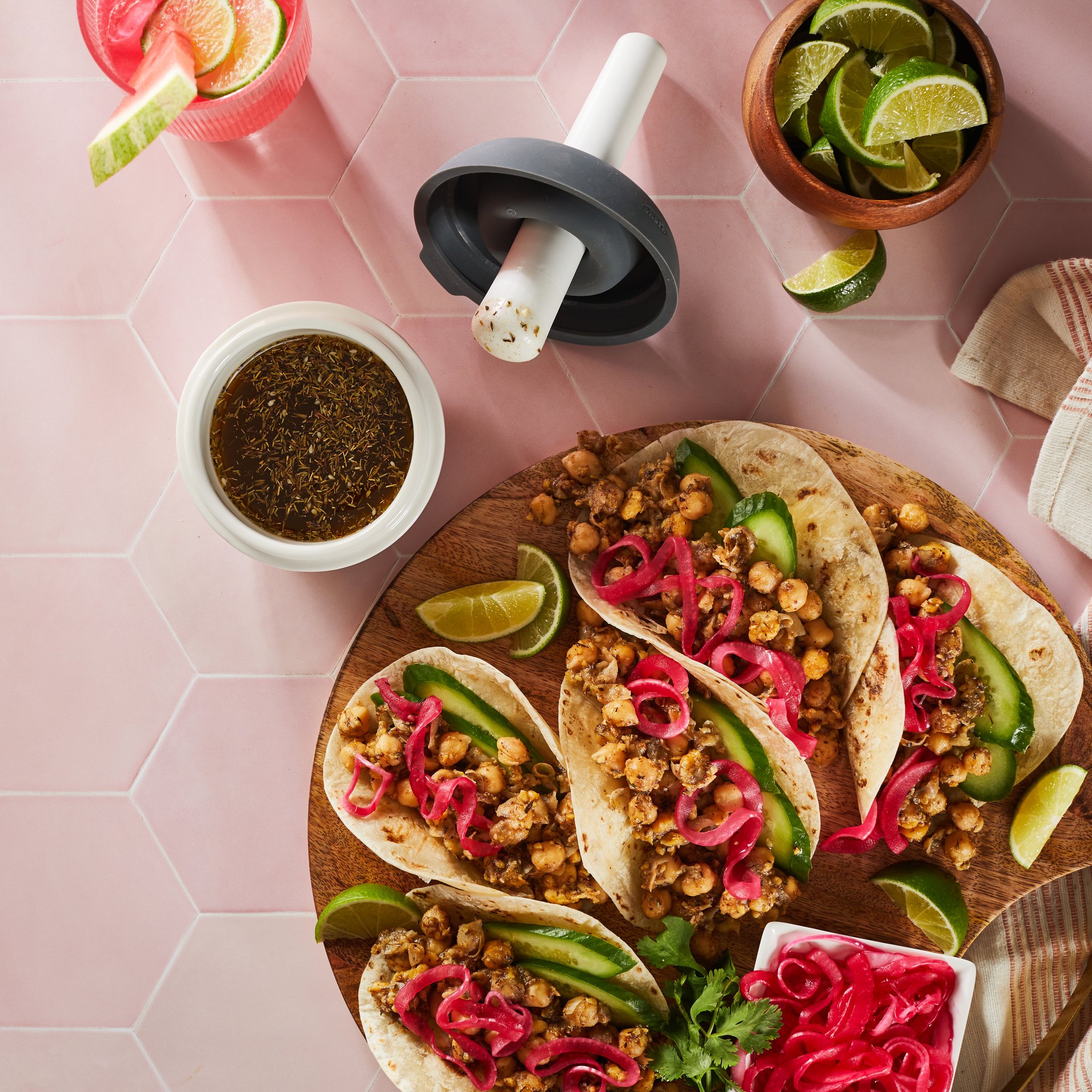 Mörser mit Gewürzmischung neben Tacos und Limetten auf rosa Fliesen