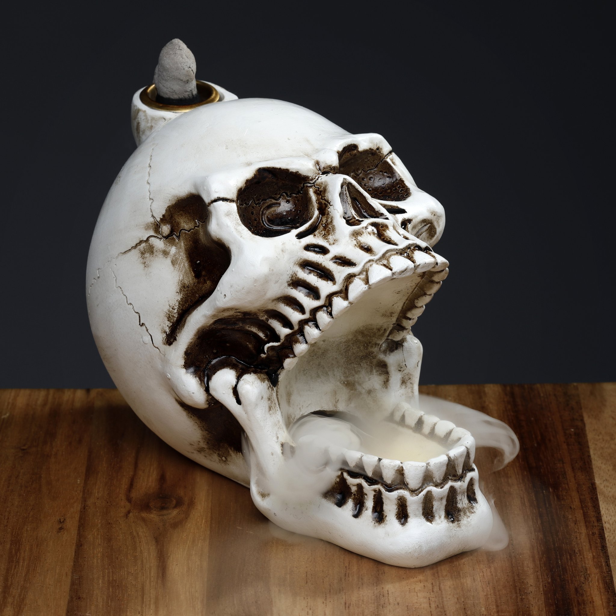 Skull incense holder on wood, smoke pouring from the skull