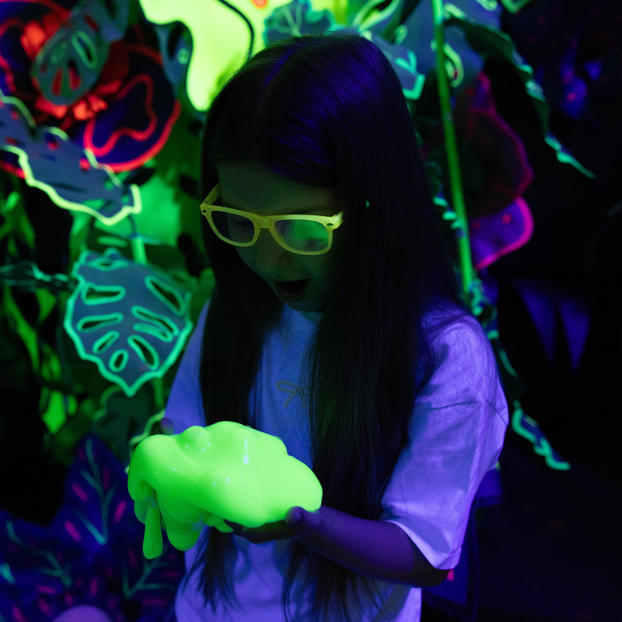 Slime verde fluorescente nelle mani di una ragazza sotto la luce nera