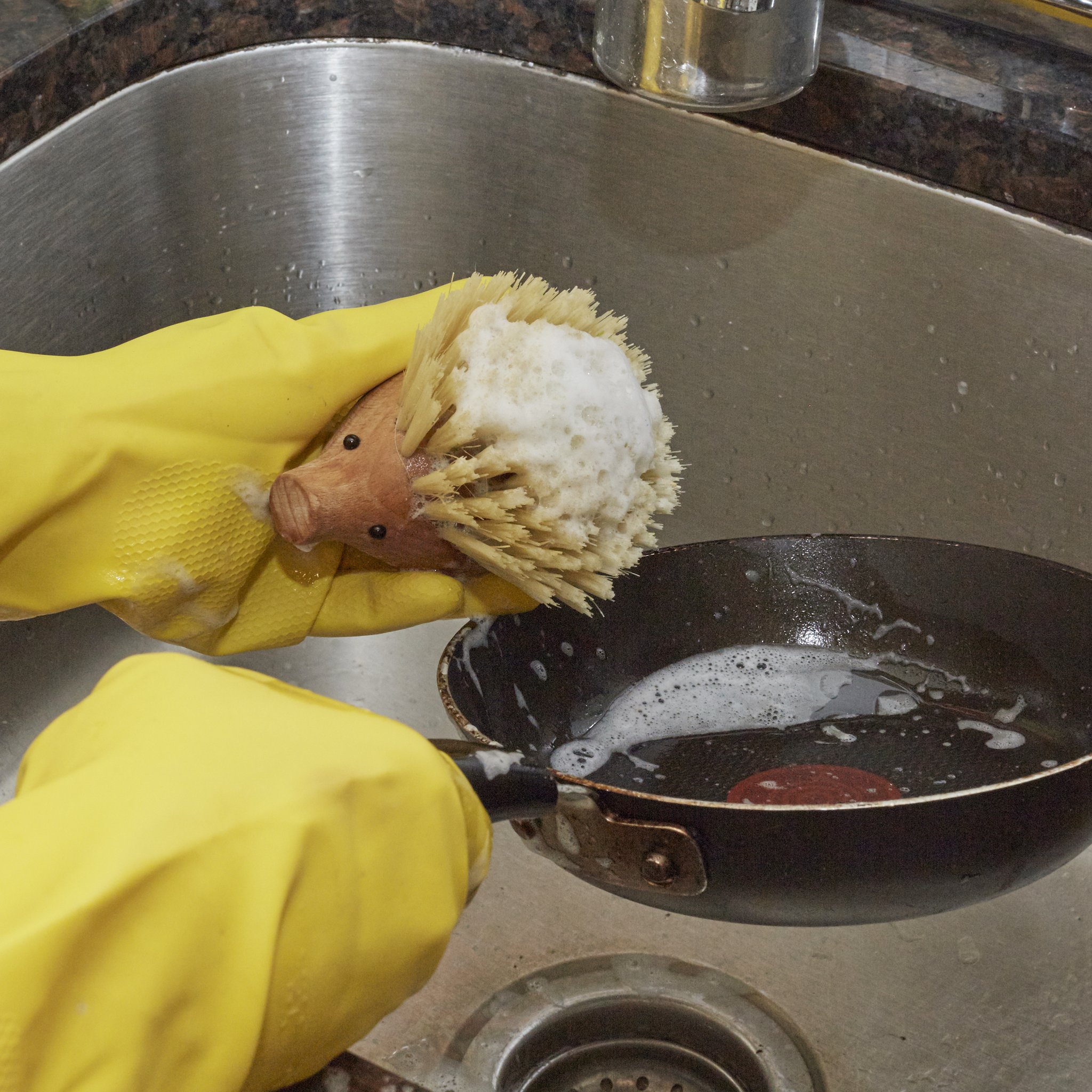 Hedgehog dish brush in yellow rubber gloves washing the pan
