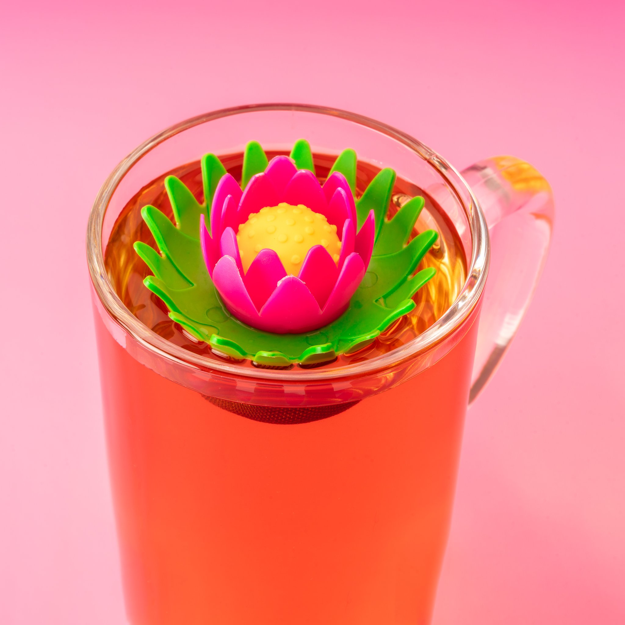 Infuseur lotus flottant dans le verre à thé sur fond rose