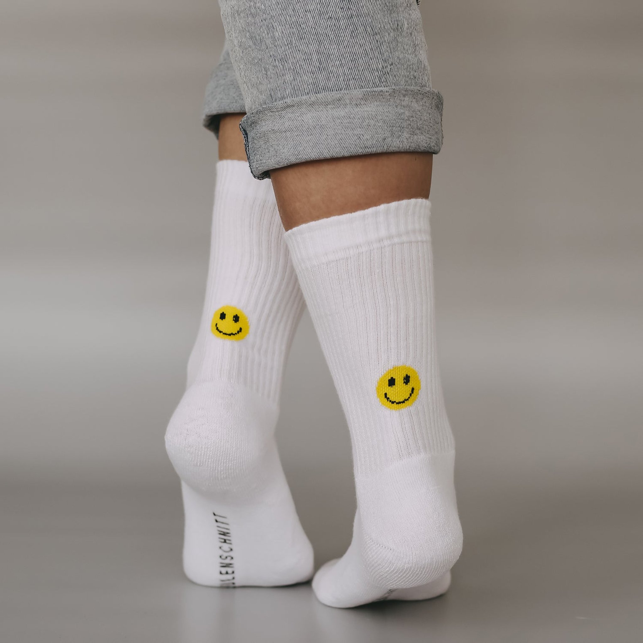 Weisse Socken mit gelbem Smiley an der Ferse, getragen vor grauem Hintergrund