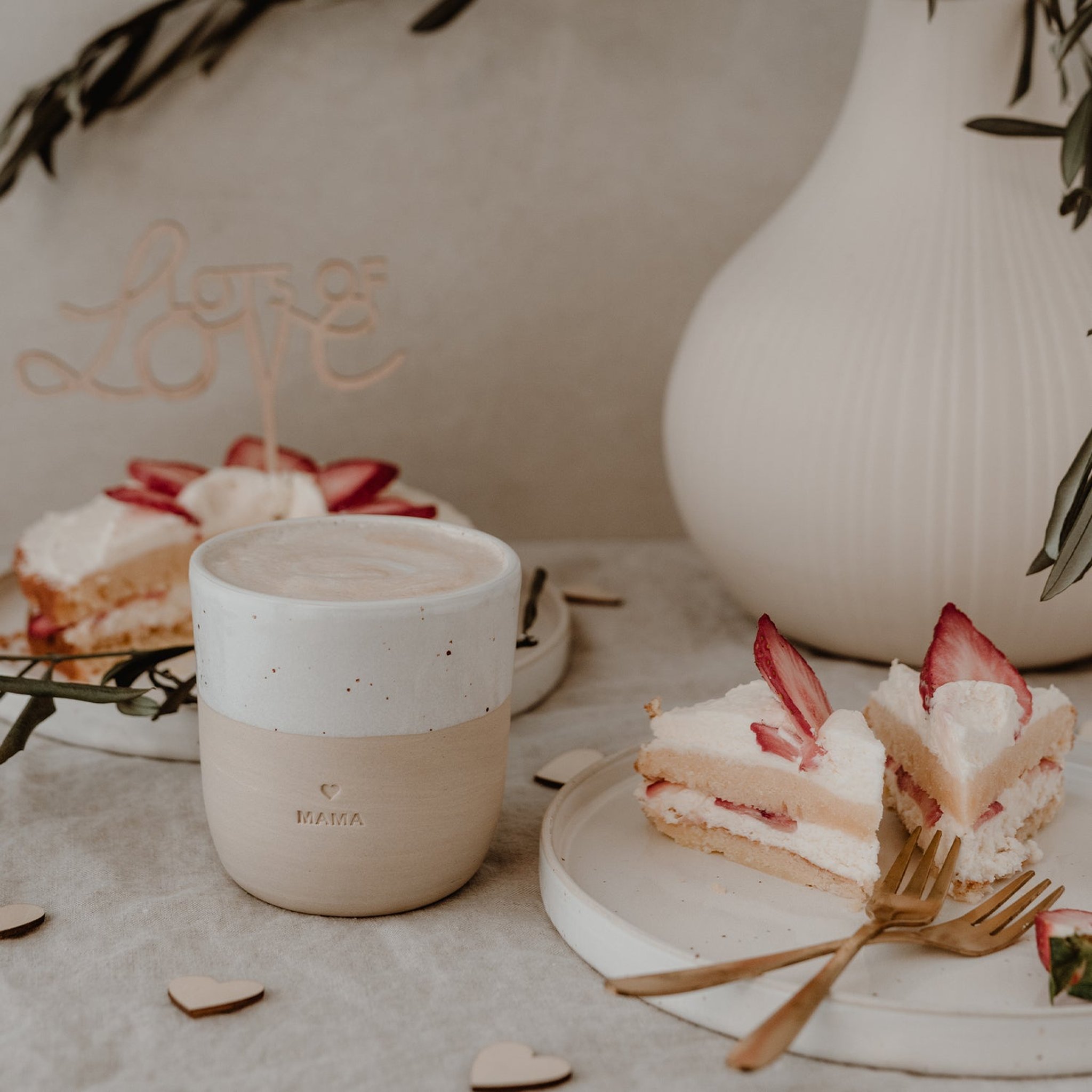 Becher Mama auf einem festlich gedeckten Tisch mit Erdbeertorte und Love-Schriftzug