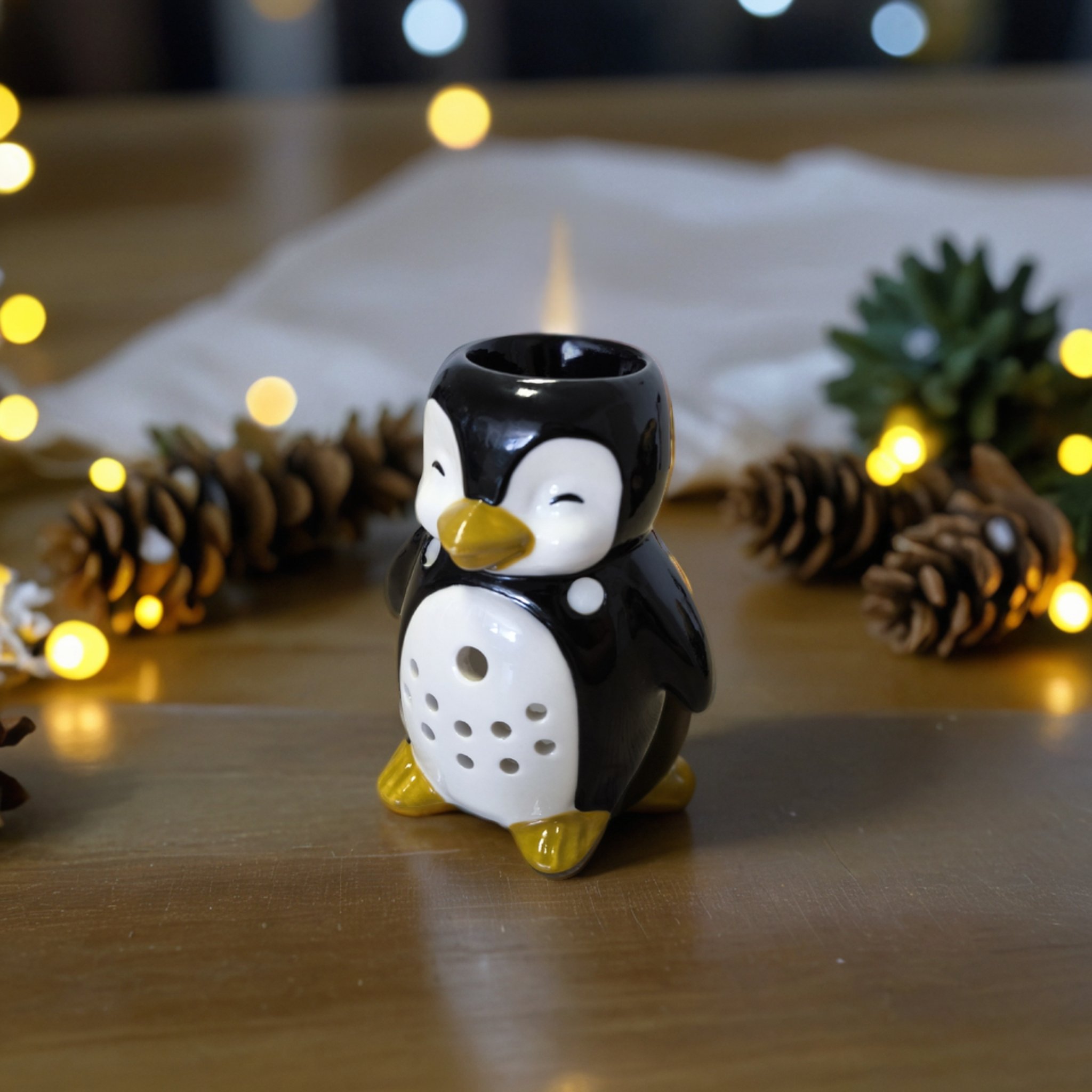 Keramik-Pinguin als Duftlampe vor Tannenzapfen und Lichterkette
