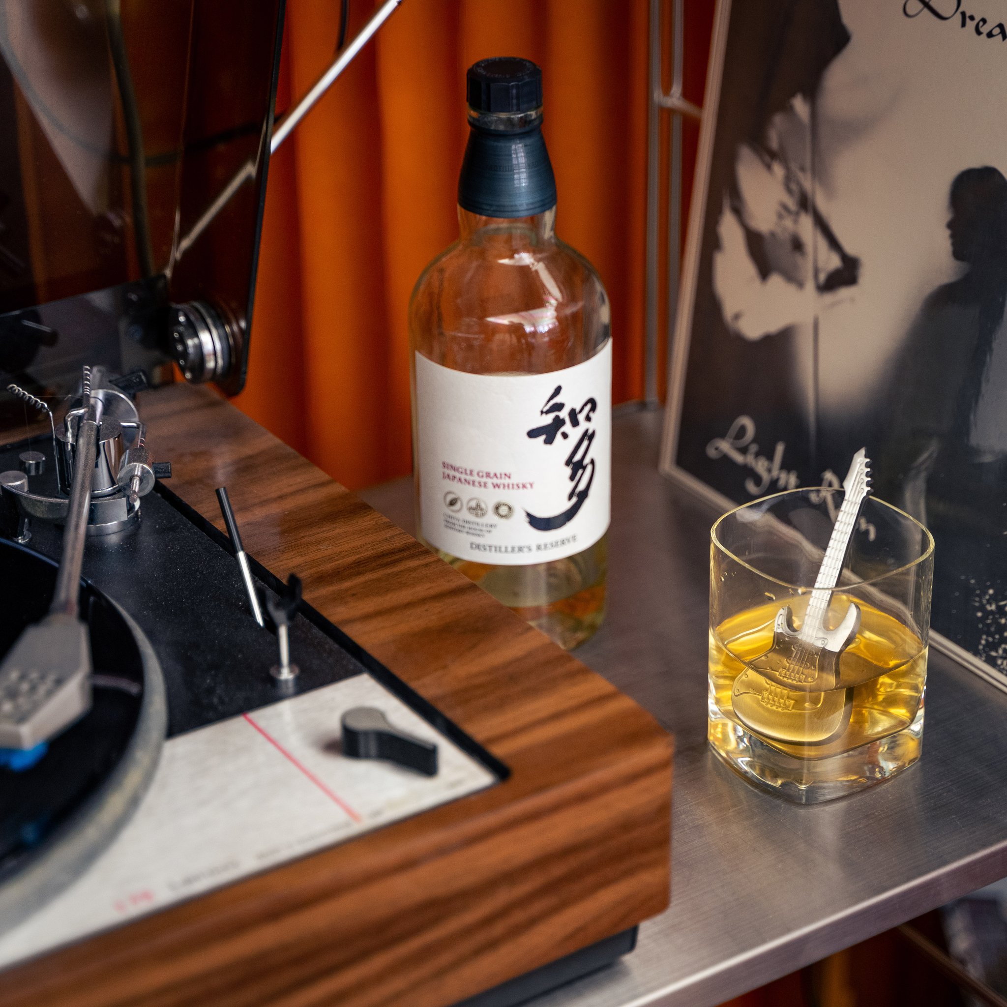 Whiskyglas mit Gitarren-Chiller neben Flasche und Plattenspieler